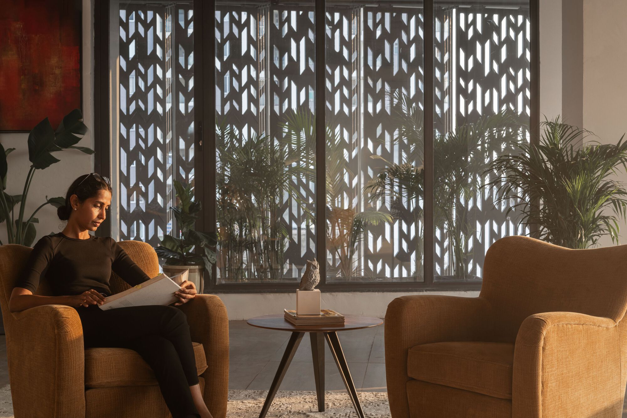 Interior seating area with decorative metal screen filtering daylight beside potted palms and upholstered chairs