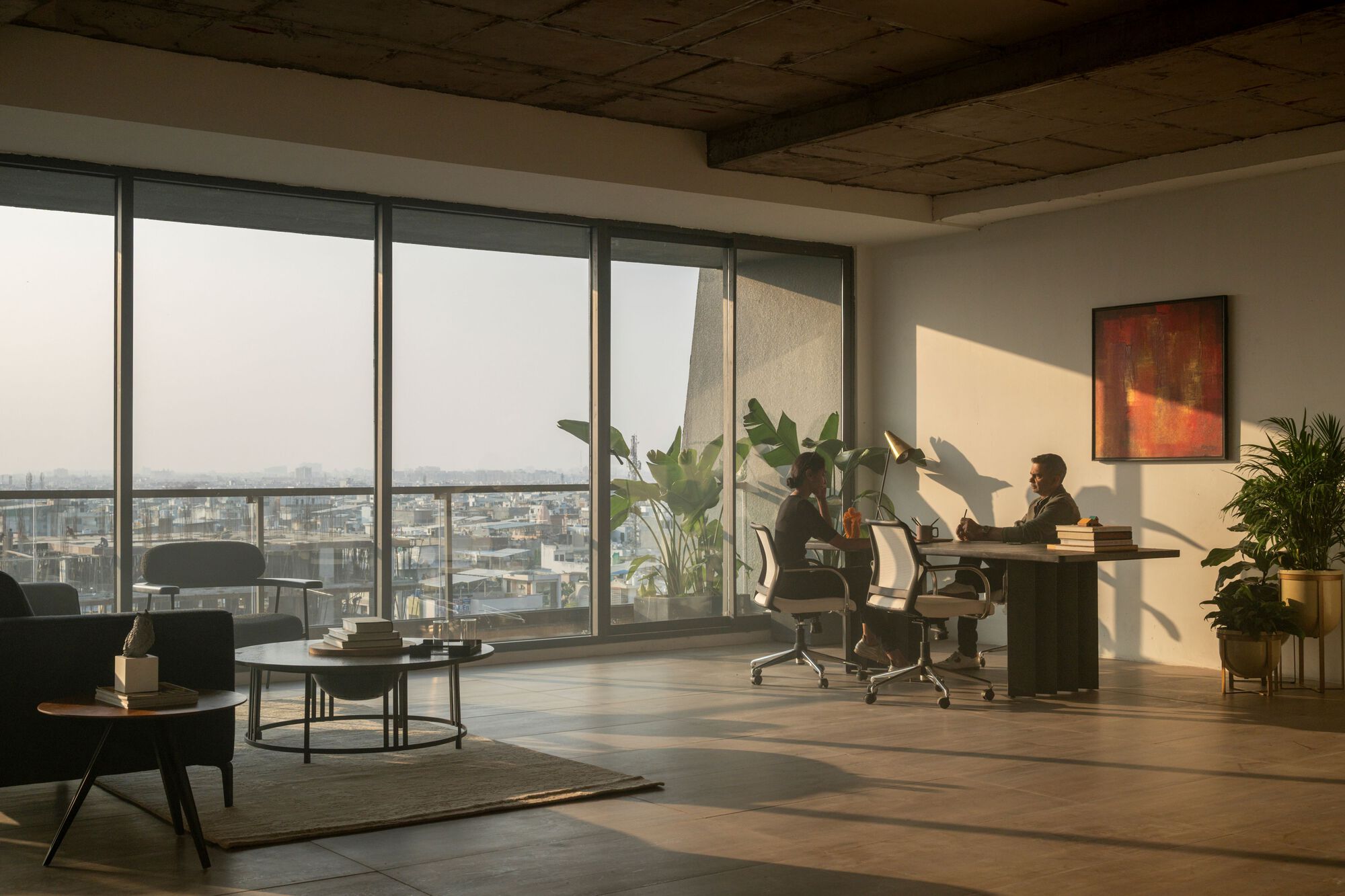 Office interior with full-height glazing overlooking the city under afternoon sun