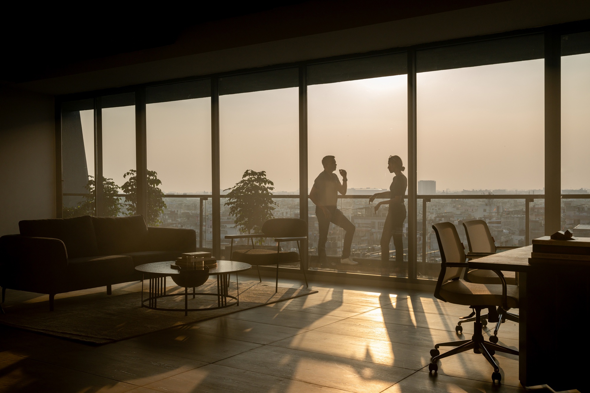 Interior balcony view at dusk with two silhouetted figures and potted plants
