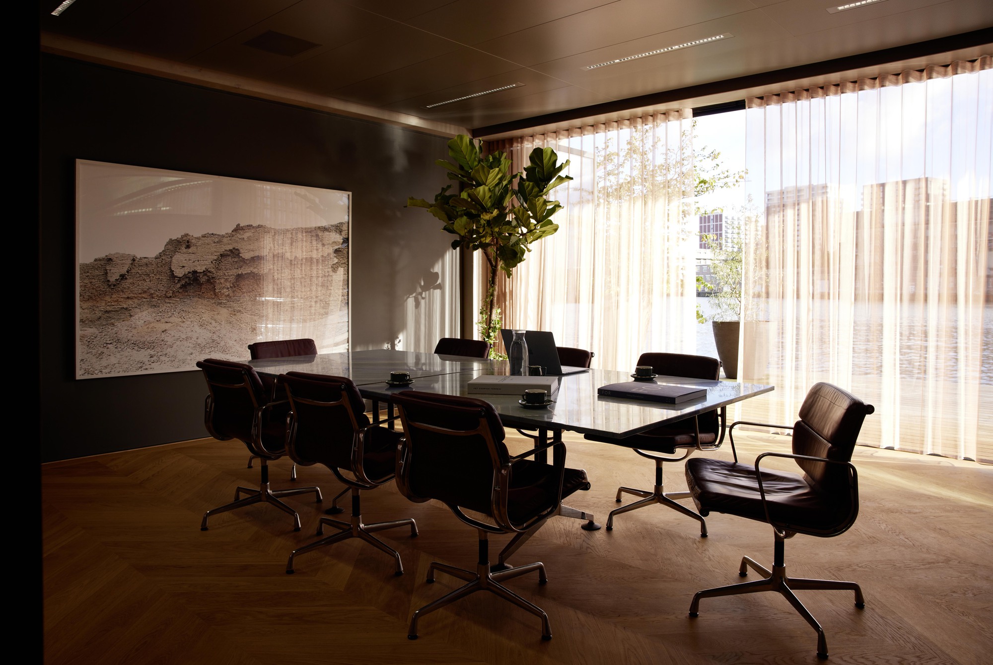 Conference room with black glass table and sheer curtains filtering daylight from floor-to-ceiling windows