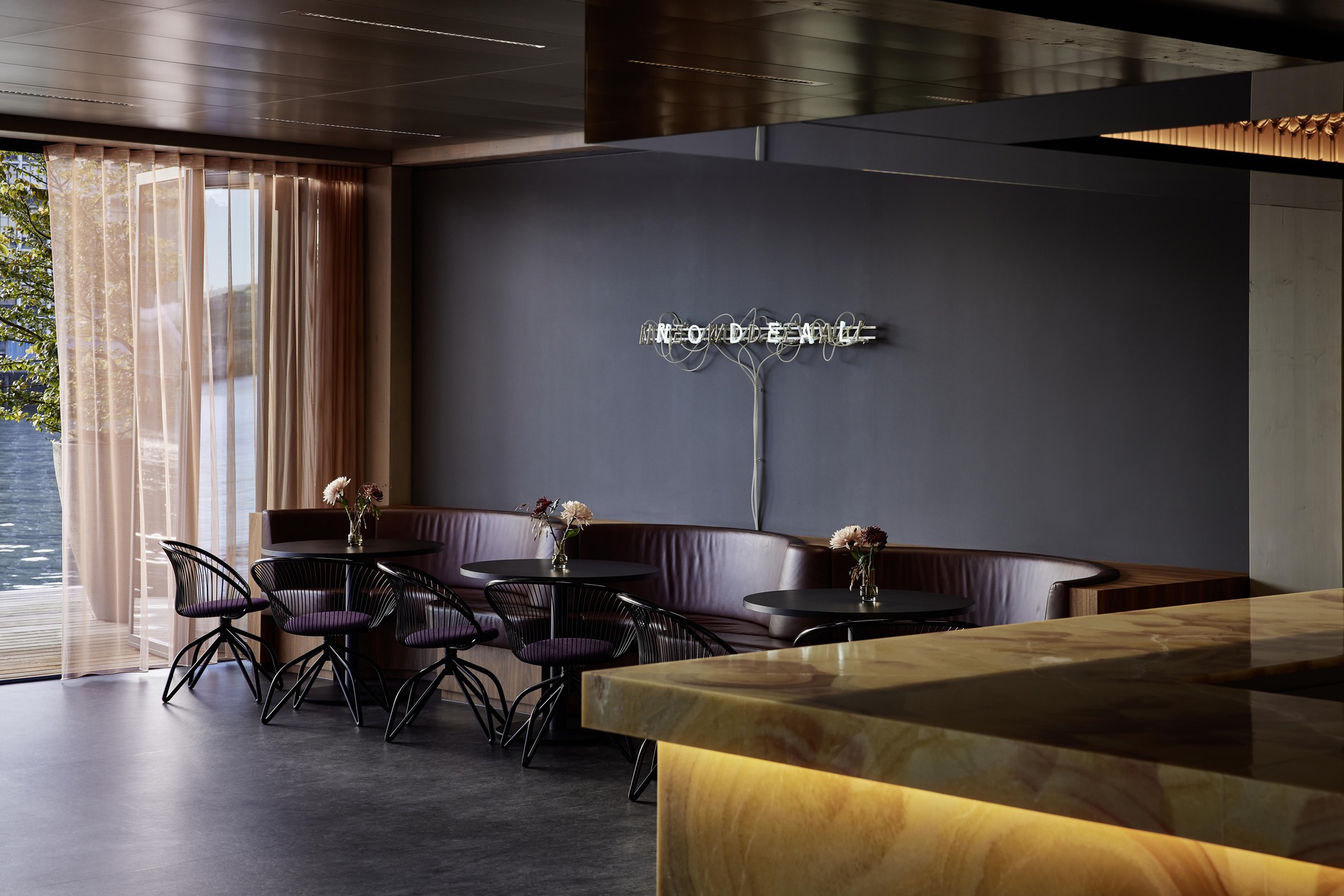Lounge seating with curved banquette and onyx service counter near curtained waterfront windows