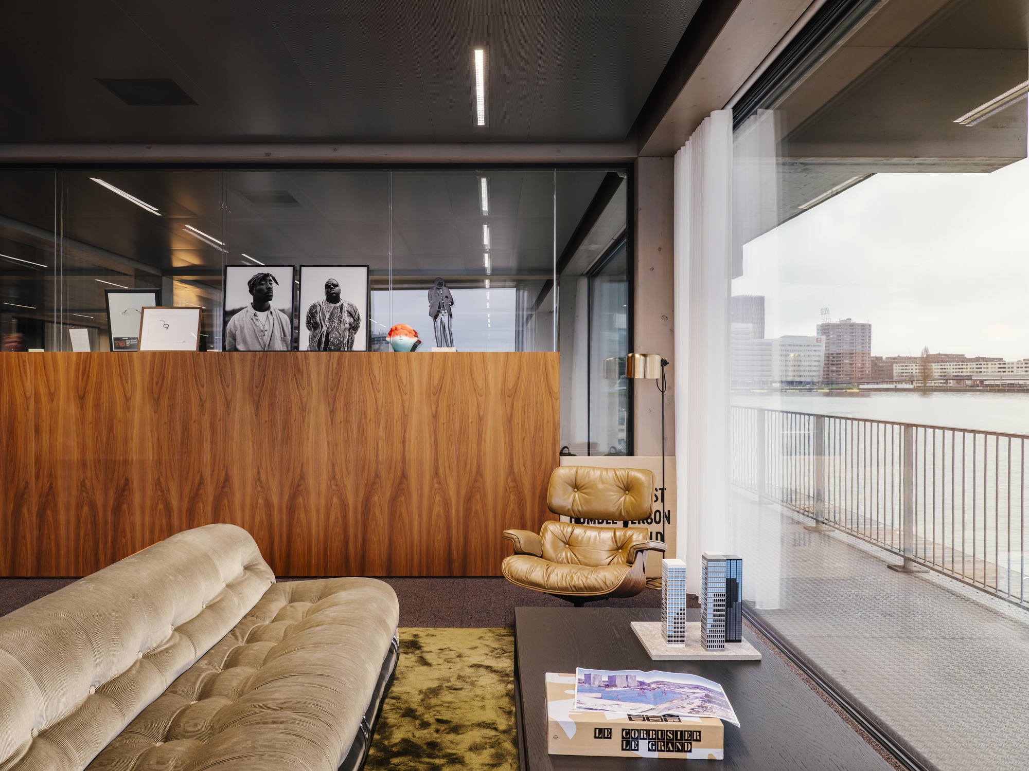 Living space with walnut veneer partition and glass walls opening to a terrace overlooking the water