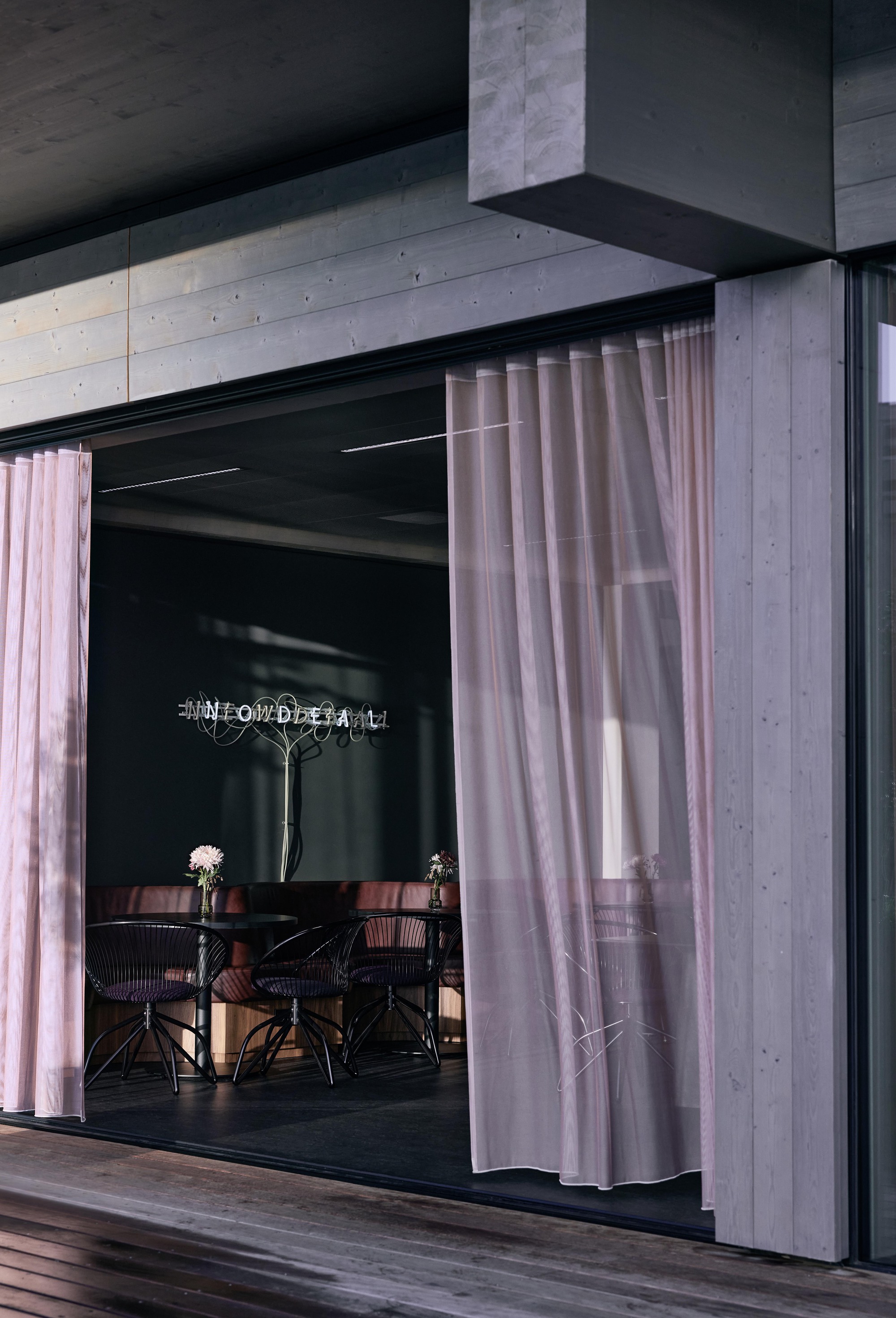 Exterior opening framed by concrete soffit and pink curtains with dining furniture visible inside at dusk