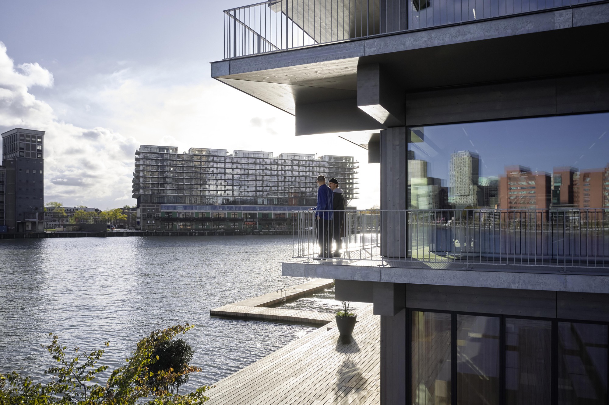 Stacked concrete balconies with metal railings overlooking the waterfront and distant buildings on a cloudy afternoon