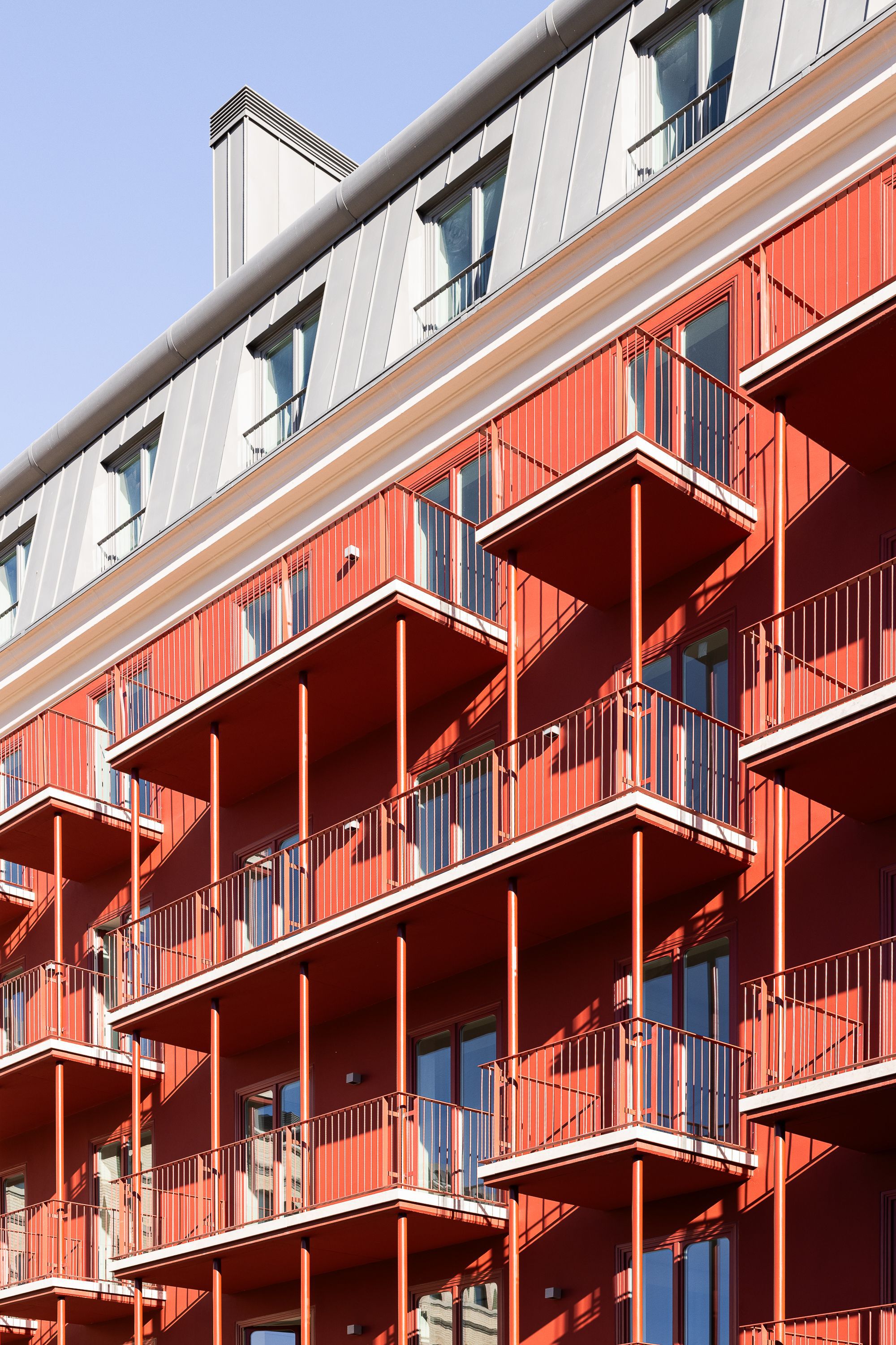 Angled red metal balconies with white trim protruding from the corrugated facade in daylight
