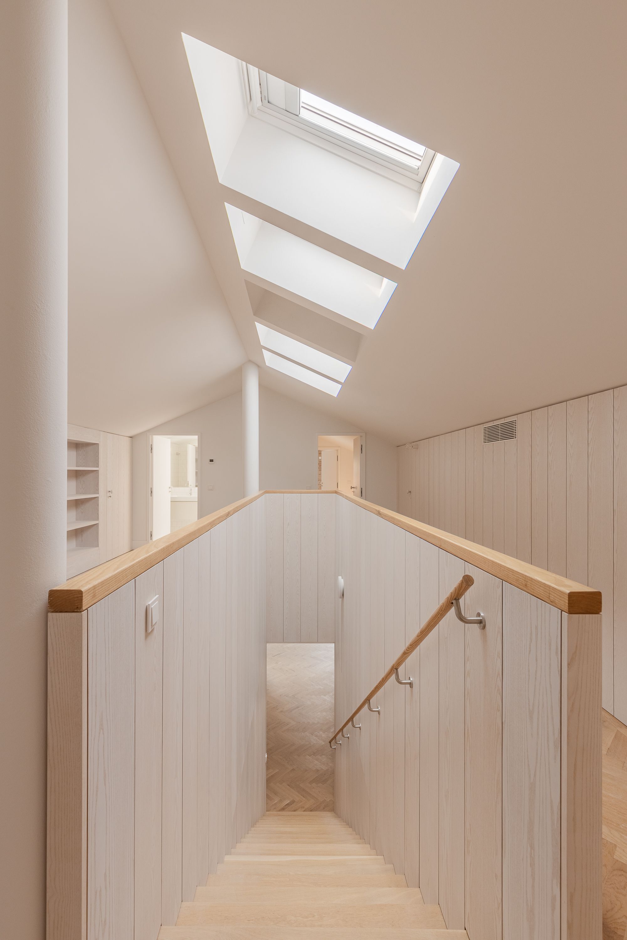 Timber staircase with vertical paneled walls ascending toward a series of skylights overhead