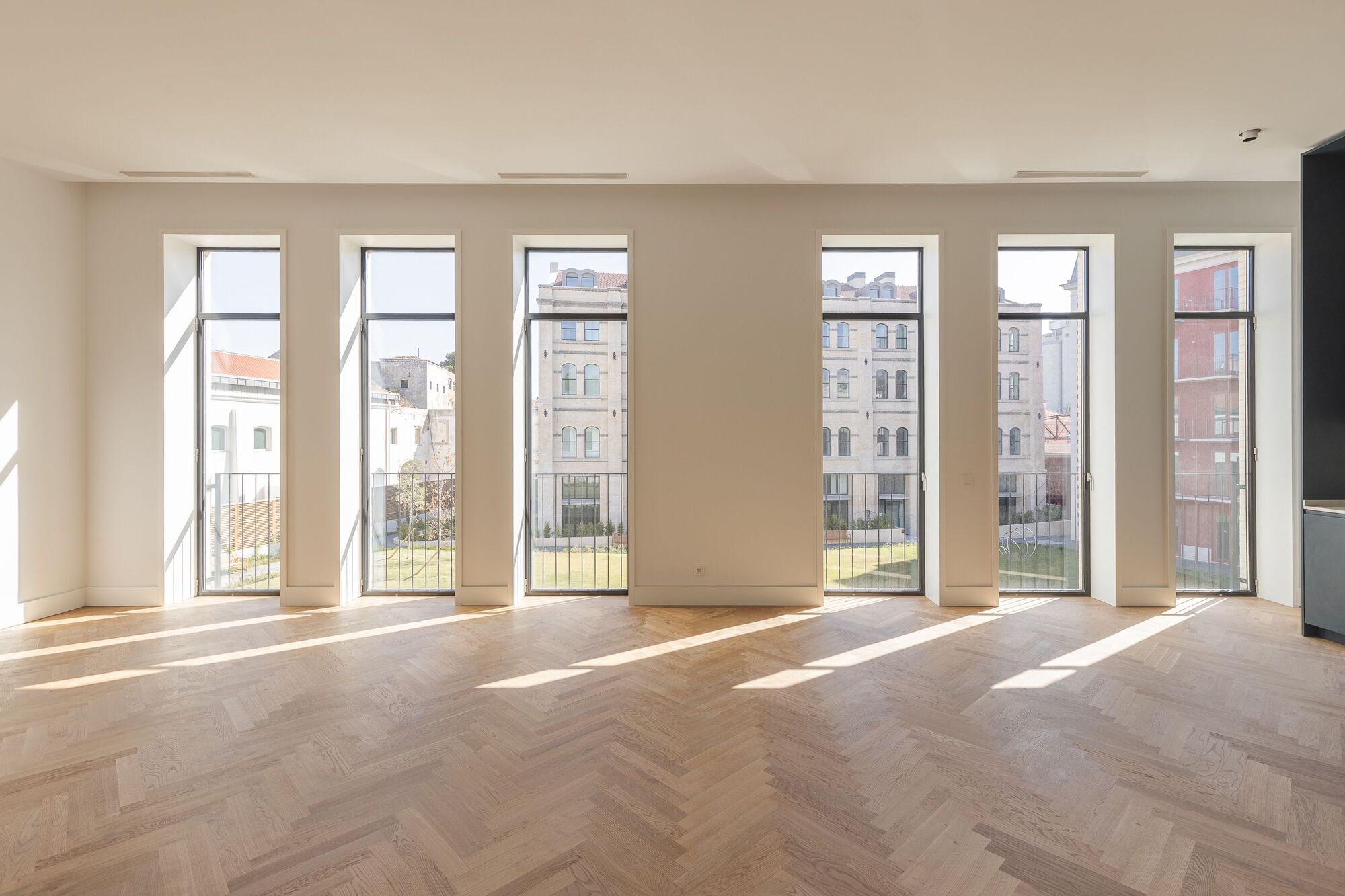 Interior with herringbone oak floor and six tall windows casting afternoon sunlight across the room