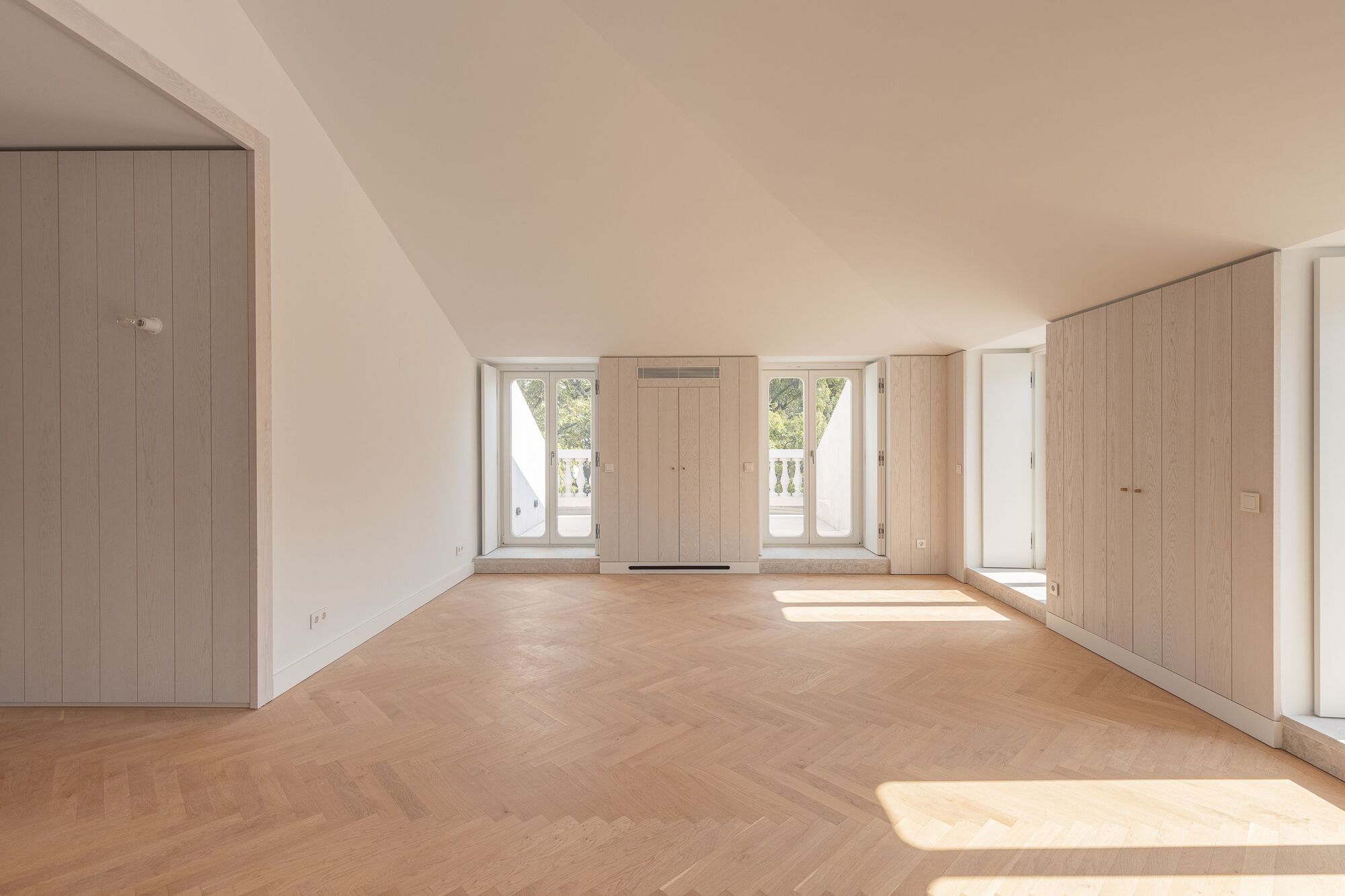 Room with sloped ceiling and light wood built-in cabinetry flanking central window