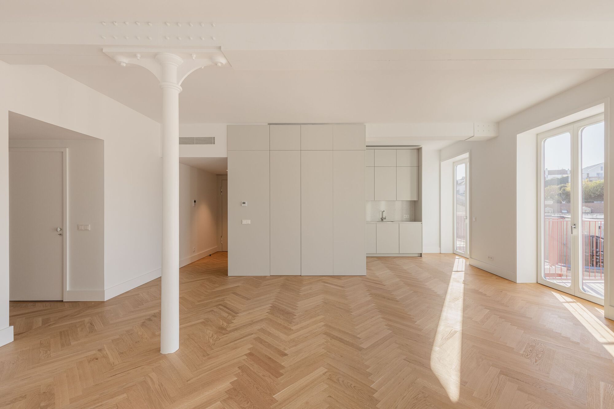 Open living space with slender white column and kitchenette volume under decorative ceiling medallion