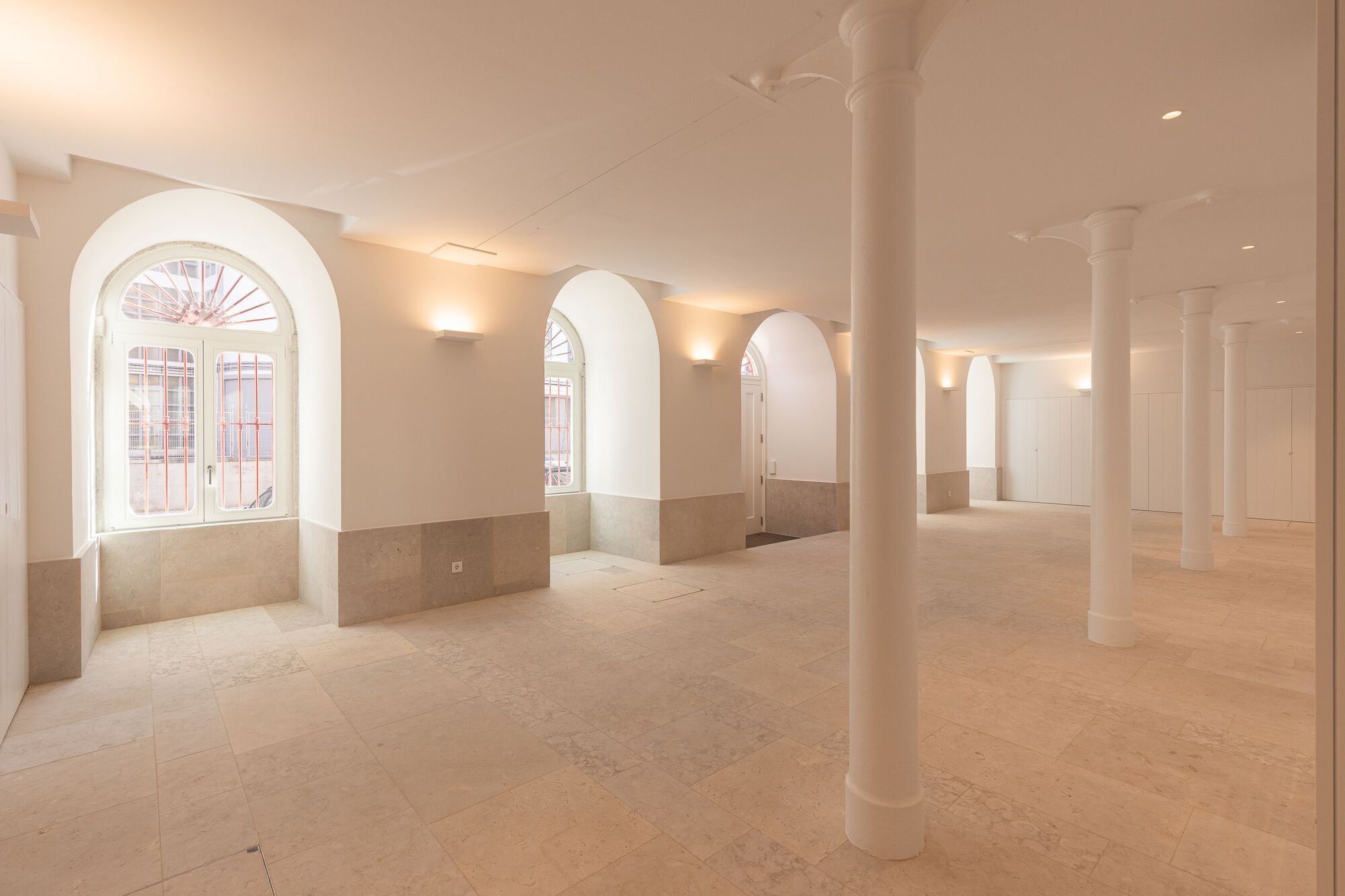 Open floor with white columns and arched windows lined with stone wainscoting in soft light