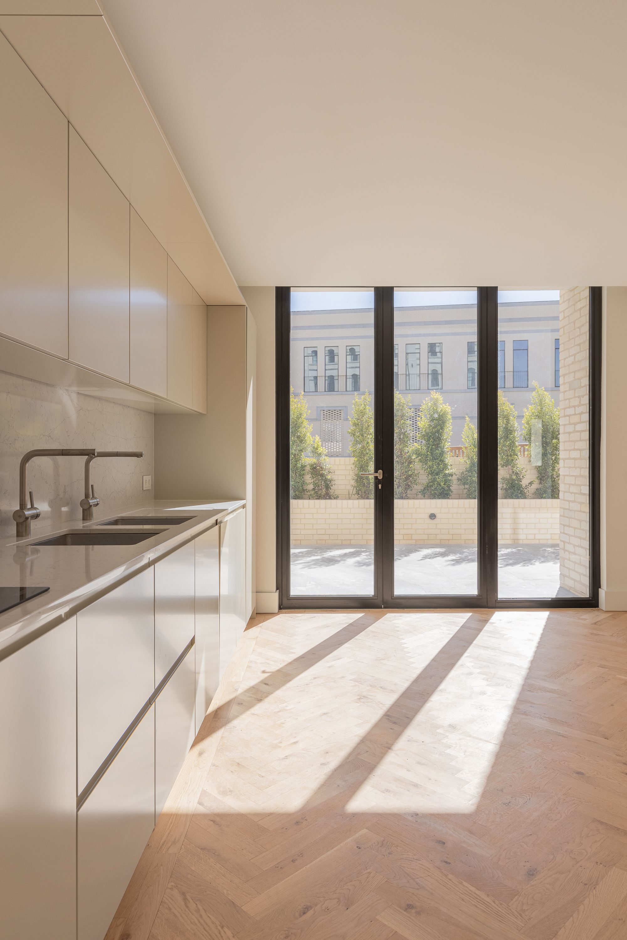 Kitchen with sloped ceiling and triple glass doors casting shadow stripes across herringbone oak flooring