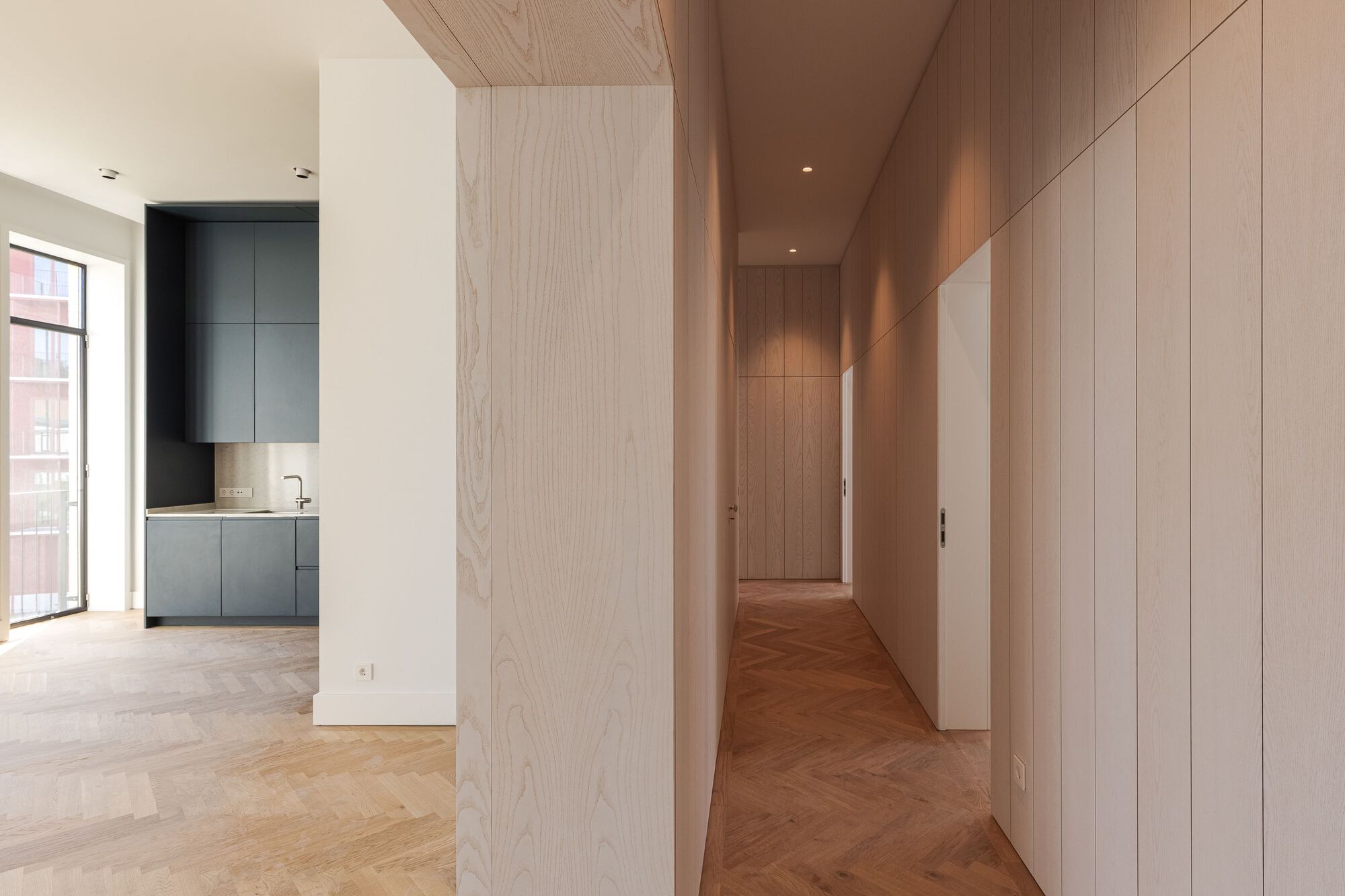 Hallway lined with timber-veneer panels and pale oak ceiling connecting rooms with herringbone wood floors
