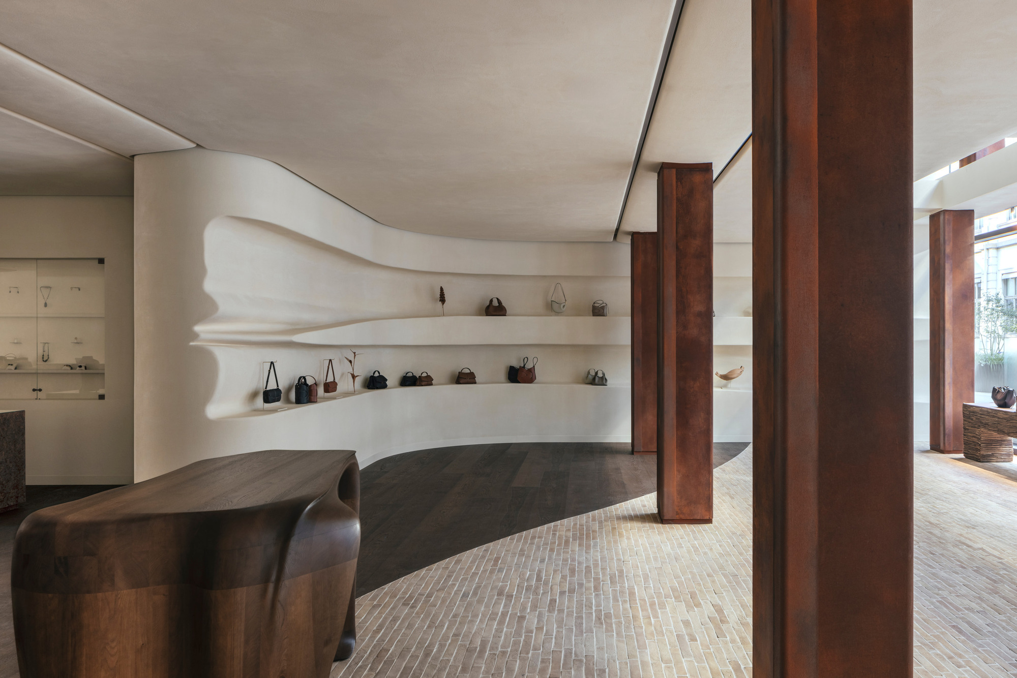 Sculpted white plaster shelving with undulating edges displaying handbags between dark timber columns