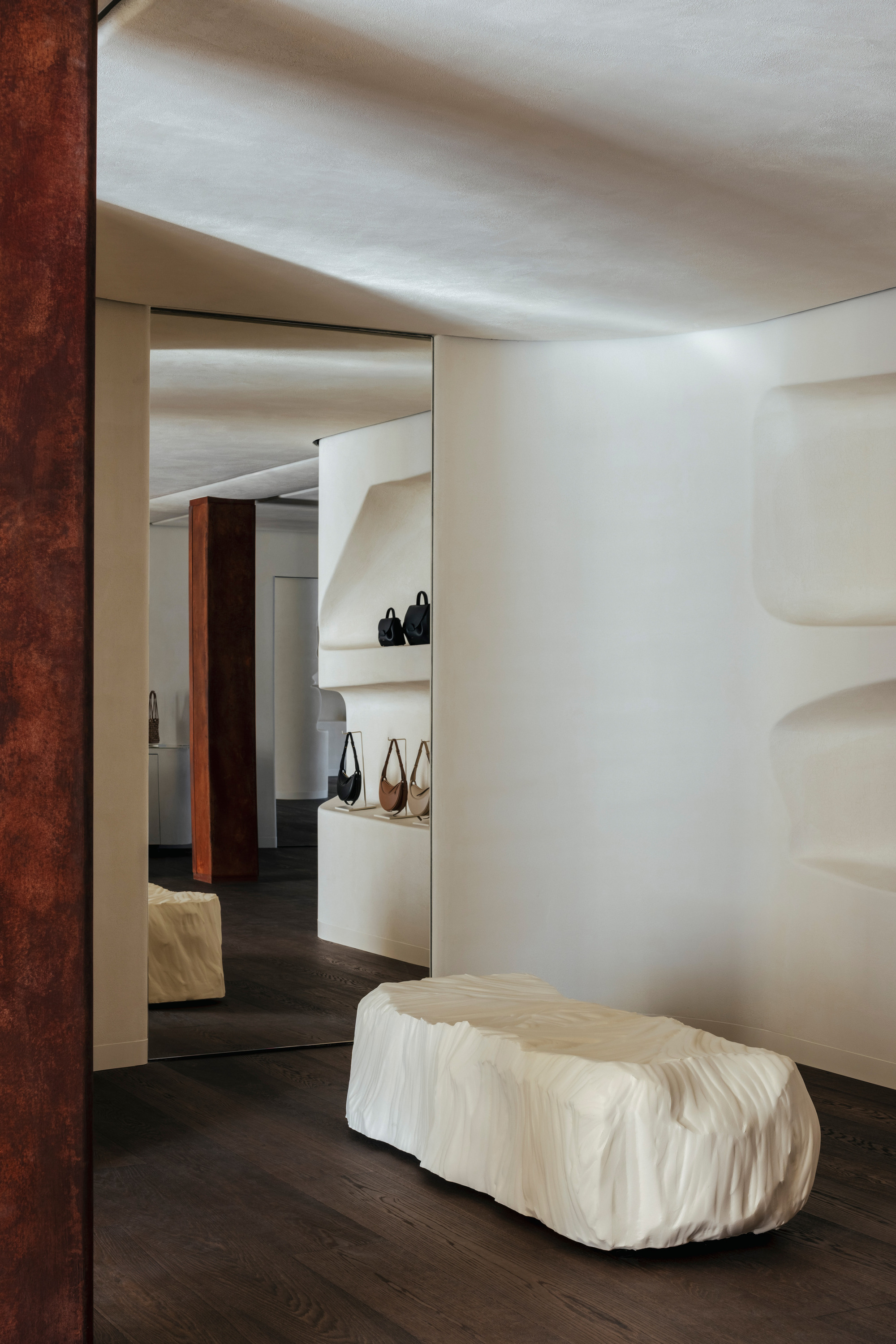 Sculpted onyx bench beneath a white plaster niche with indirect lighting and framed doorway beyond