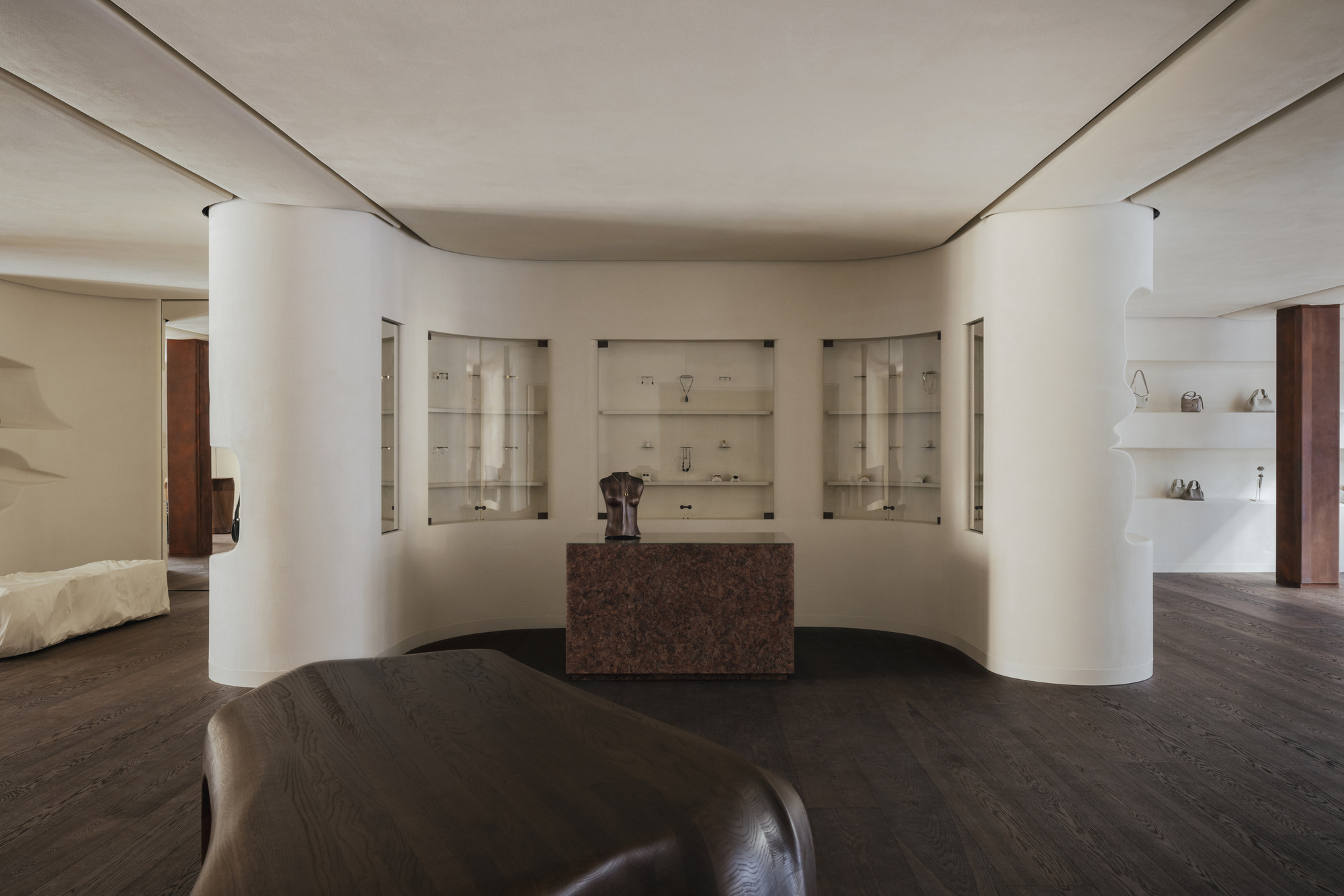 Curved wall with recessed glass vitrines flanking a central red granite counter beneath indirect cove lighting