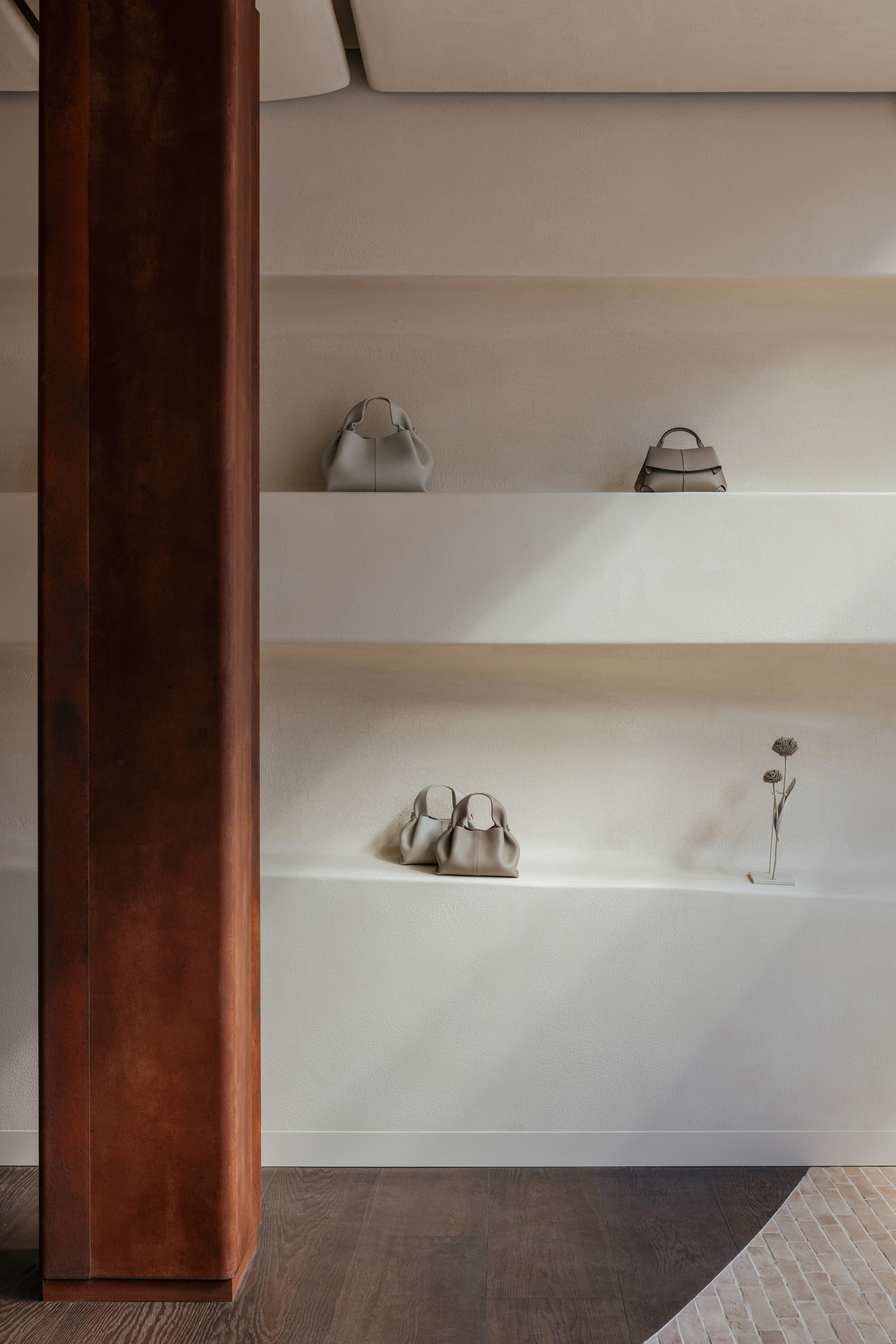 Detail of white floating shelves displaying merchandise beside a dark timber column in soft natural light