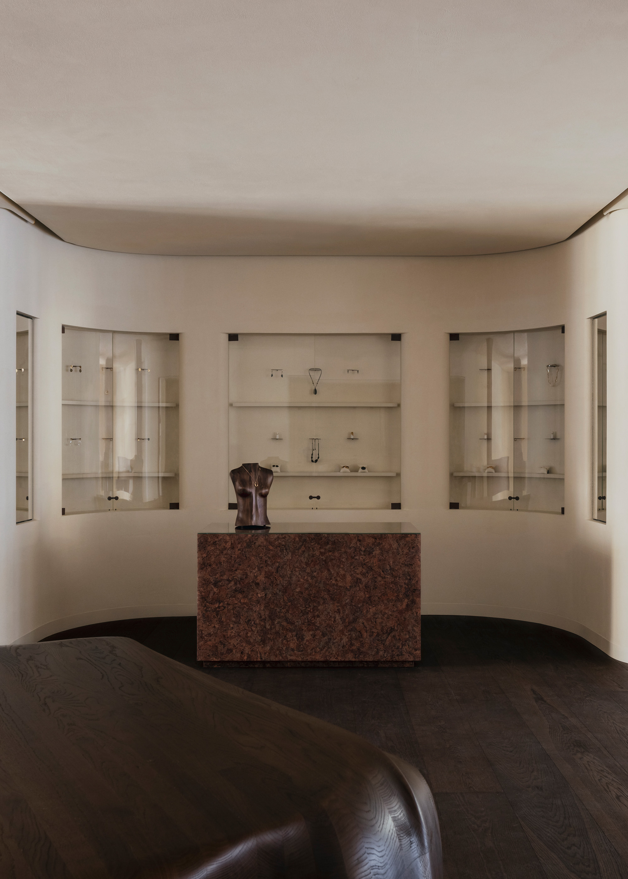 Symmetrical view of curved wall with illuminated vitrines and red granite counter on dark timber flooring