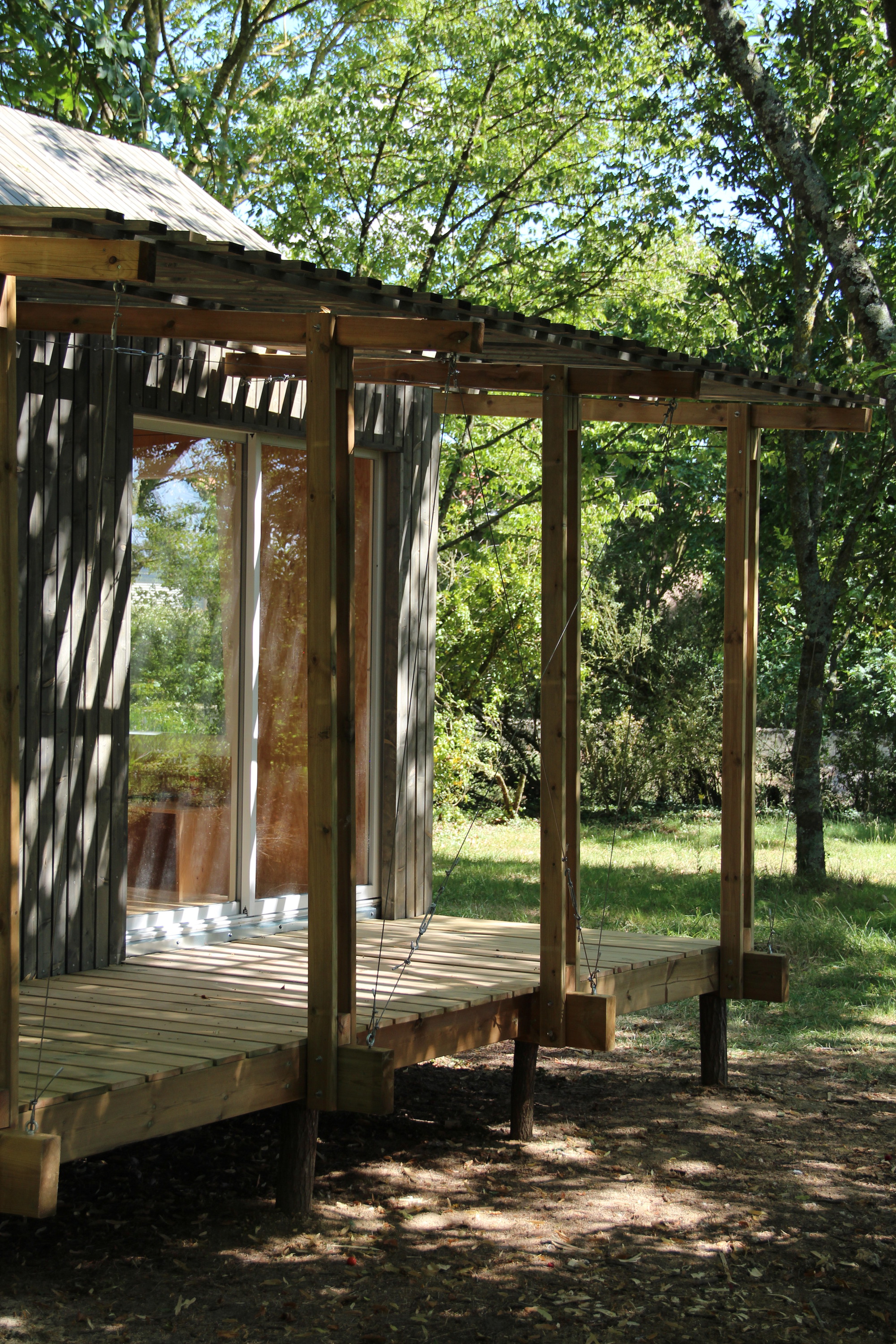 Timber-framed pavilion with exposed rafters and decking beneath dappled tree canopy