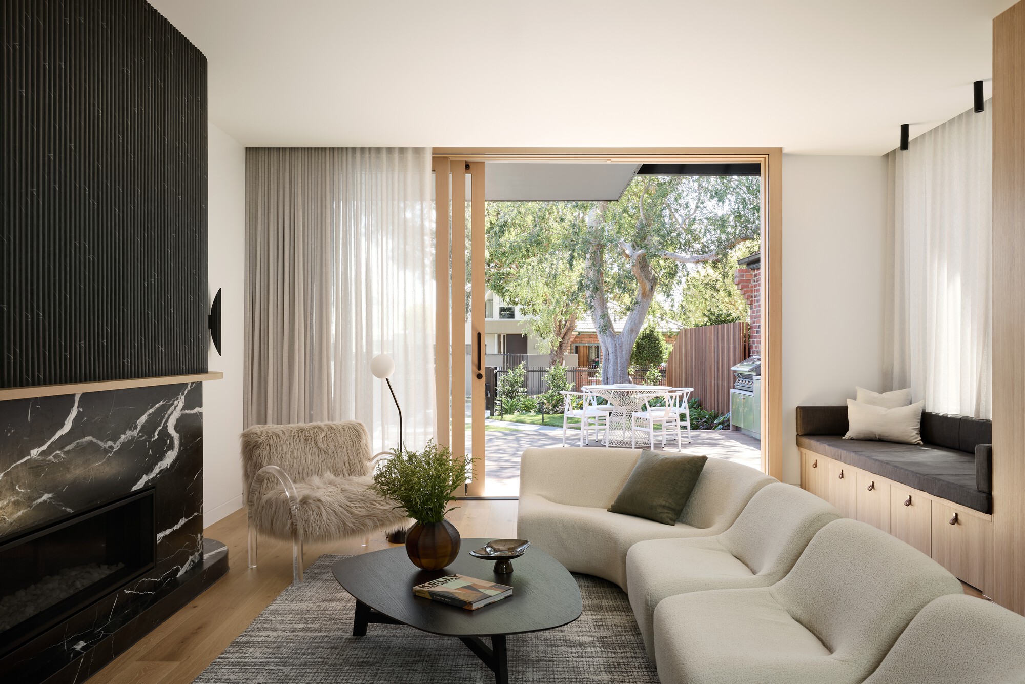 Living room with sheer curtains framing a timber-lined door opening to the garden and outdoor terrace beyond