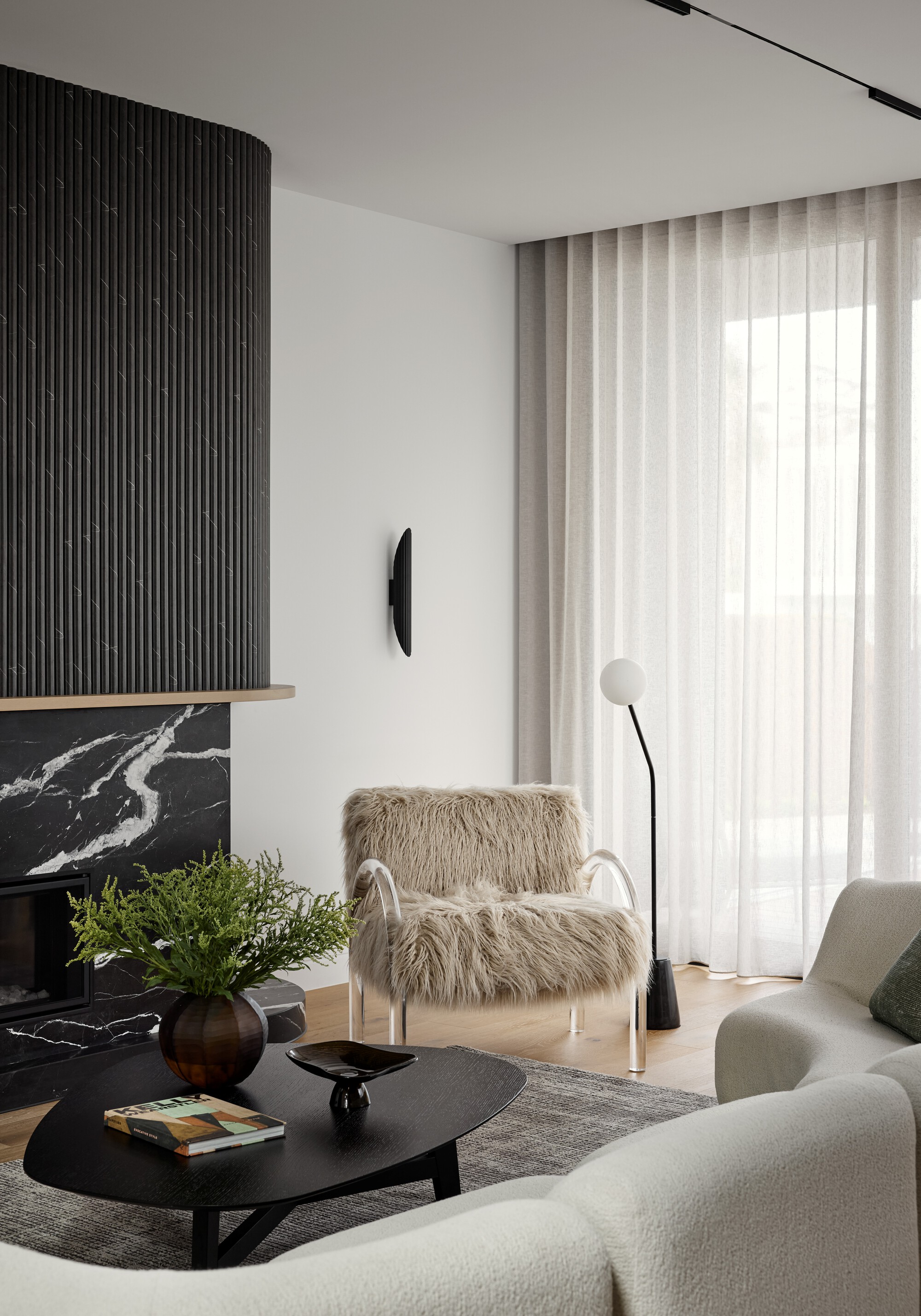 Living room fireplace surround in black marble with vertical batten hood and sheer curtains filtering daylight