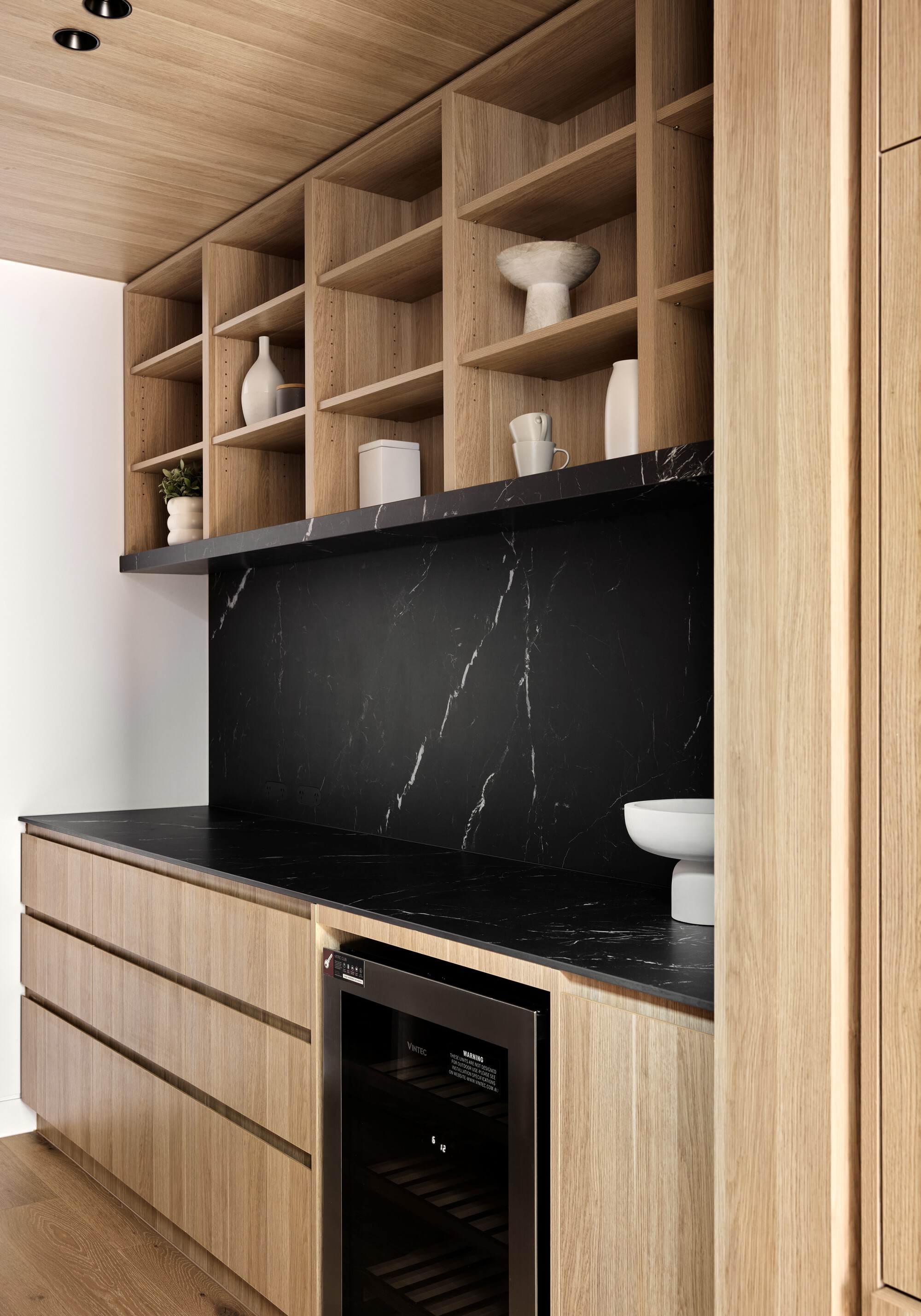 Timber open shelving above black marble counter with built-in wine refrigerator