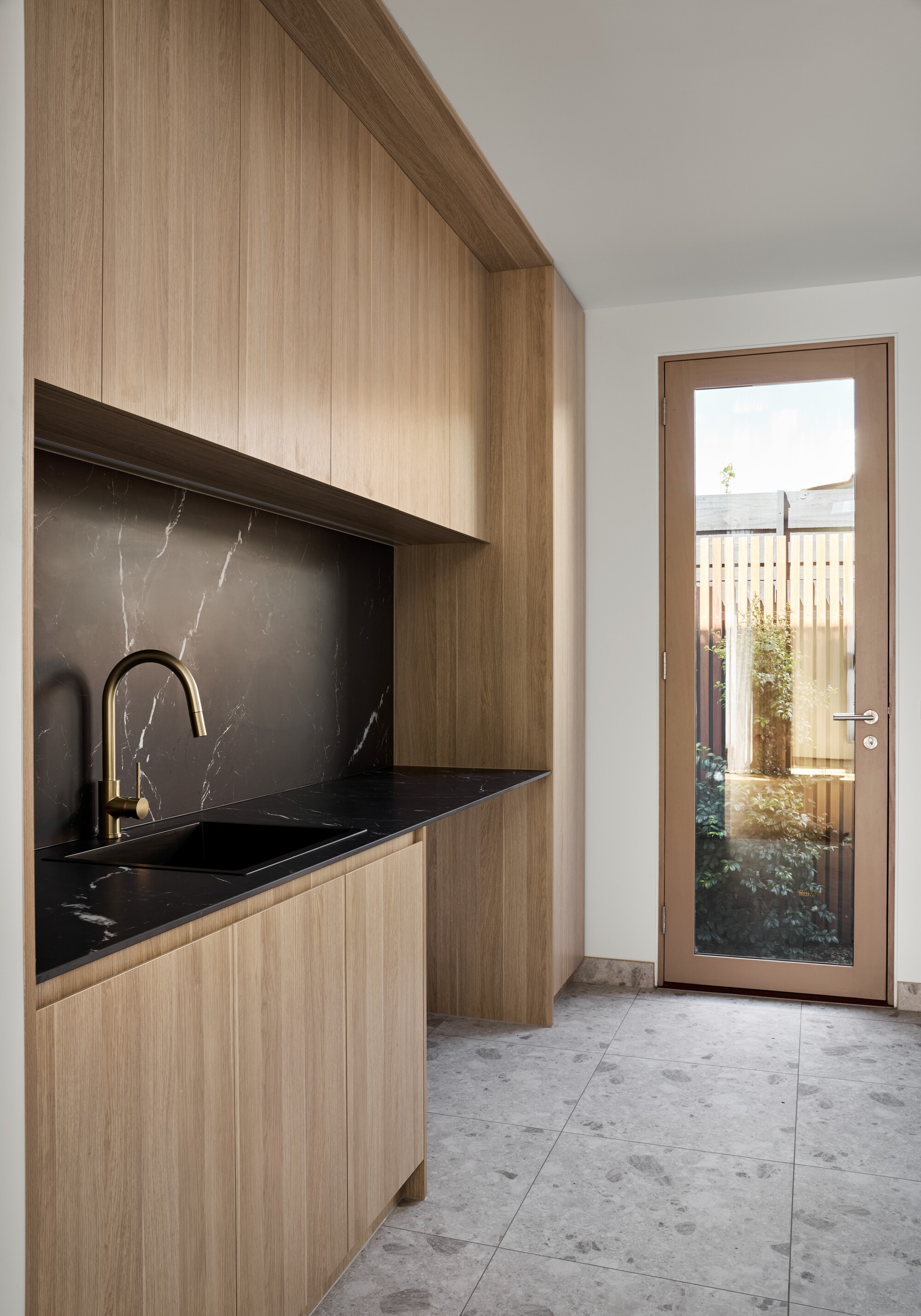 Timber cabinetry with black stone countertop and backsplash beside a glazed door to a planted courtyard