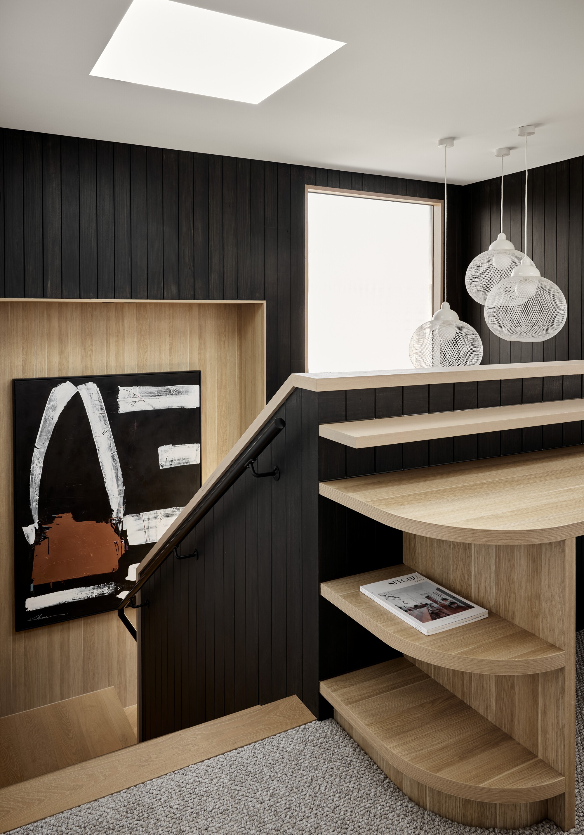 Curved timber stair treads against a black vertical panel wall with mesh pendant lights overhead