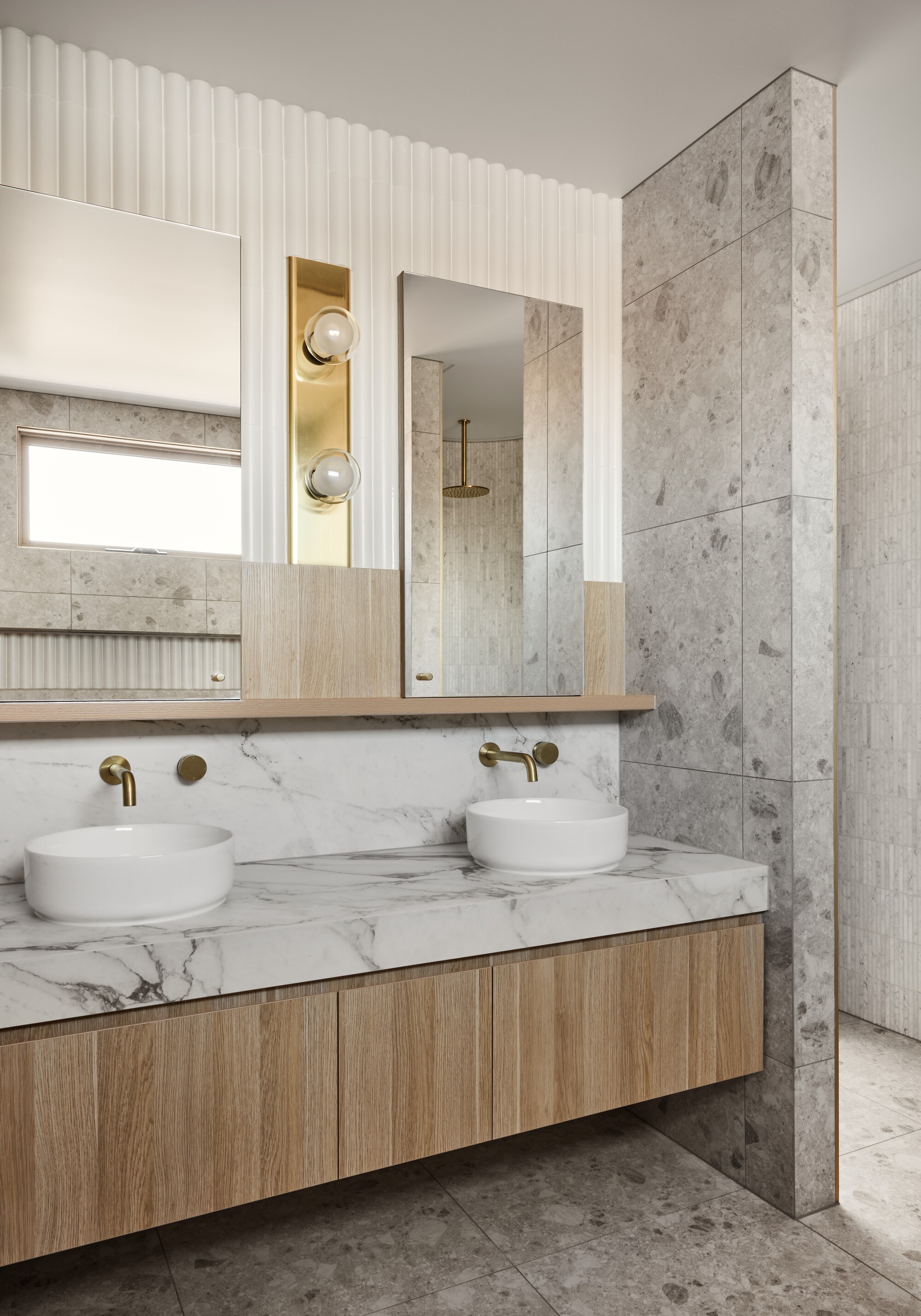 Double basin vanity with marble top and timber cabinet beneath tall mirrors and brass sconces