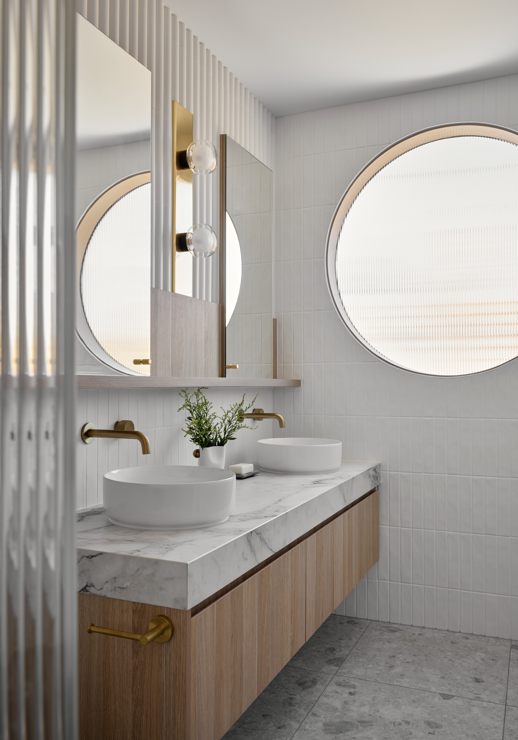 Twin circular mirrors with timber frames above a marble vanity and vessel sinks with brass fittings