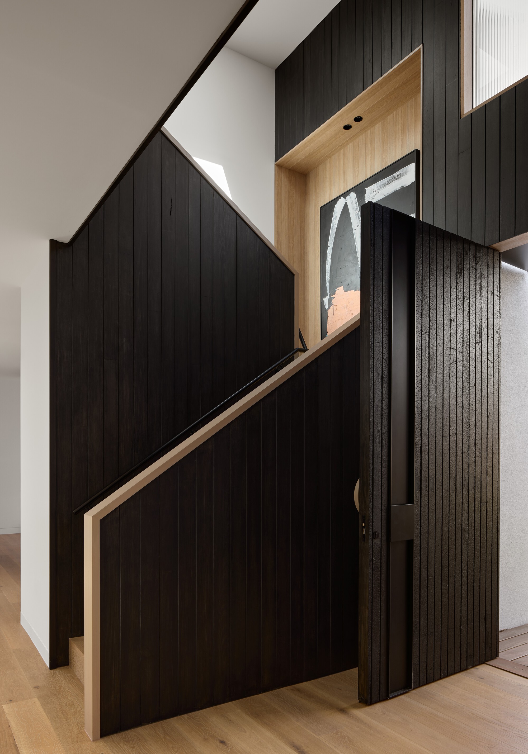 Understairs storage with black cladding and timber-lined display niche beneath angled stair soffit