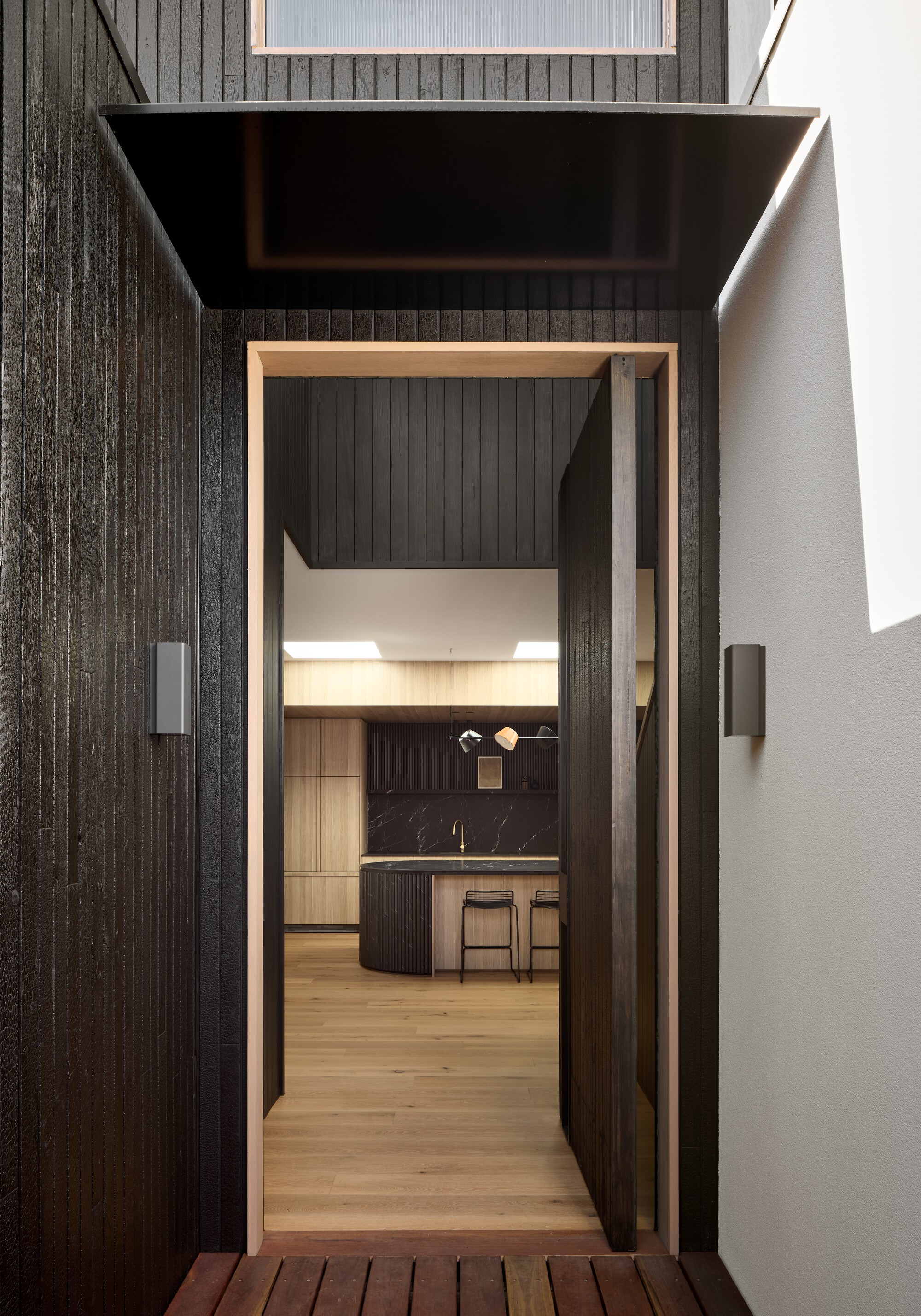 Doorway with timber frame opening from timber deck to kitchen with black island and skylights