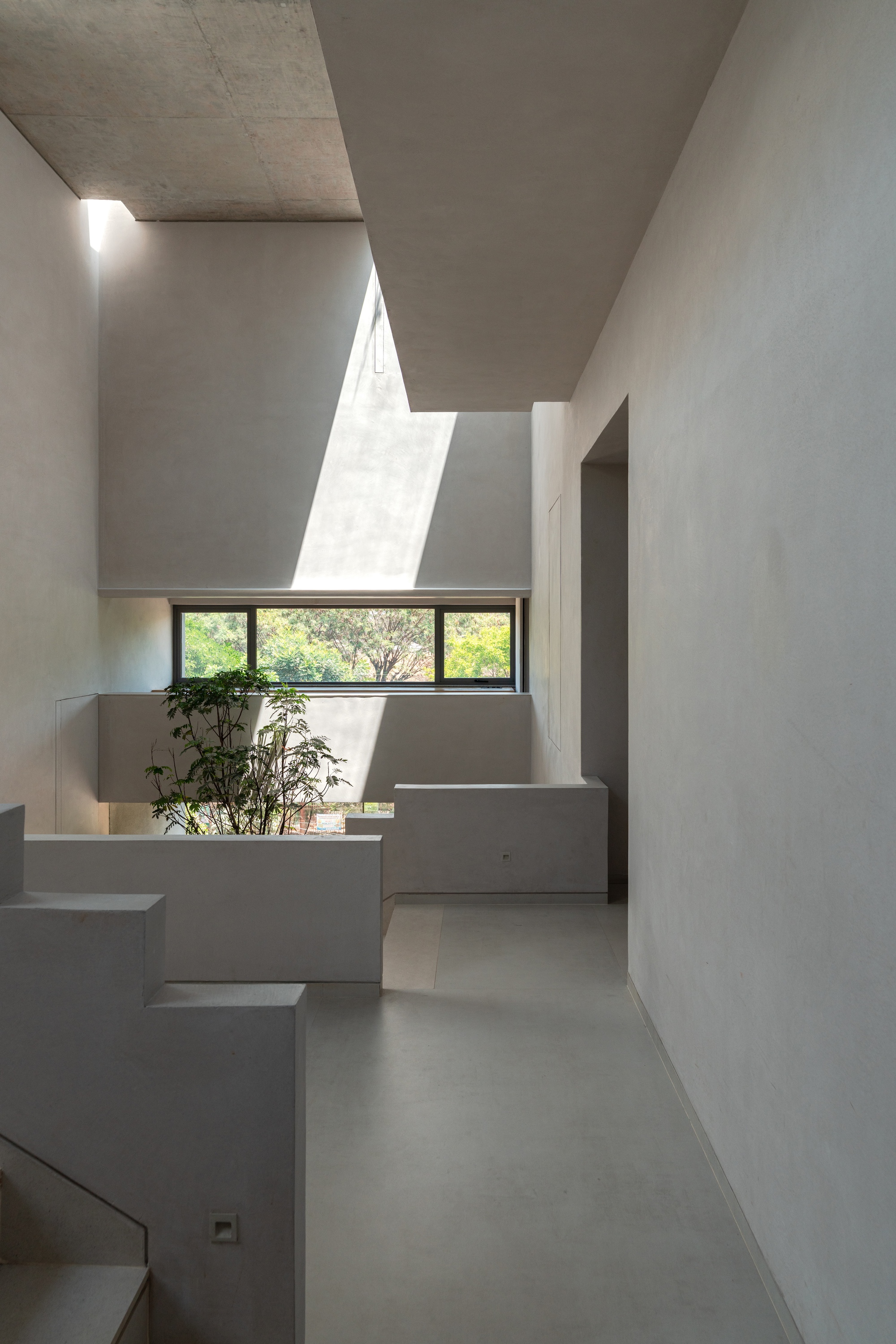 Narrow hallway with concrete ceiling and horizontal window framing greenery outside