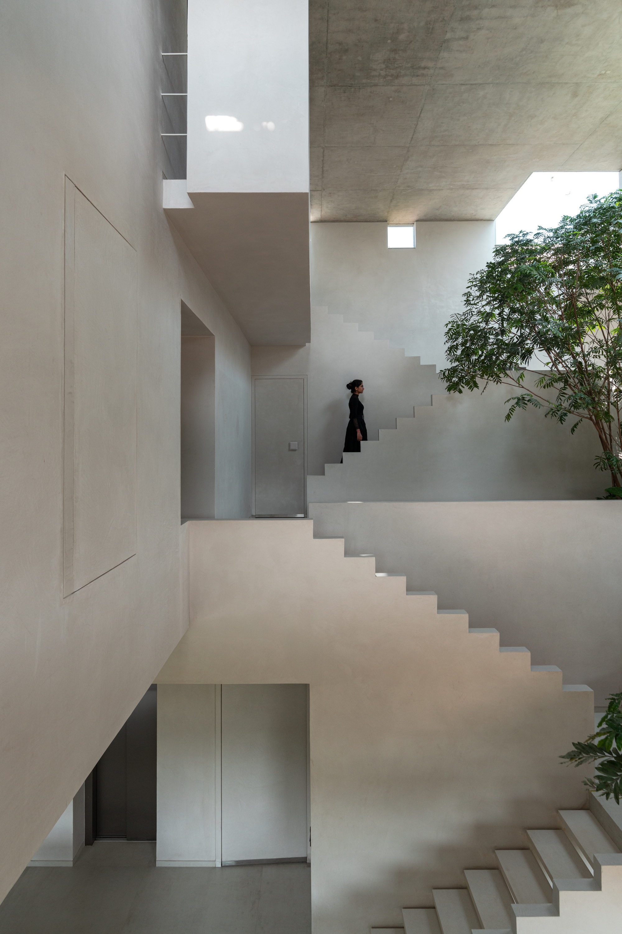 Interlocking white stairs around a planted courtyard with a figure ascending the upper flight
