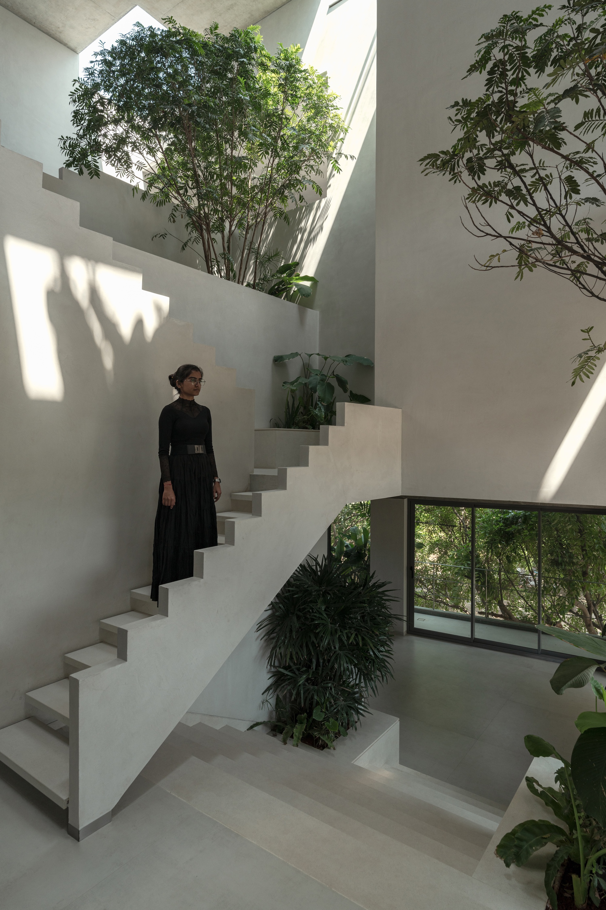 Figure in dark clothing standing on the cantilevered staircase illuminated by dappled sunlight from the tree canopy