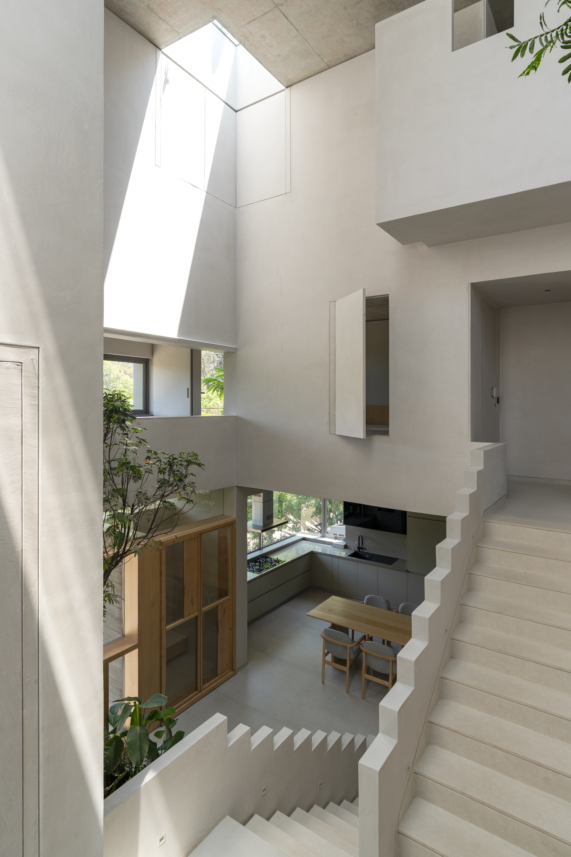 Vertical atrium view showing stacked levels connected by staircases with an angled skylight shaft bringing daylight down