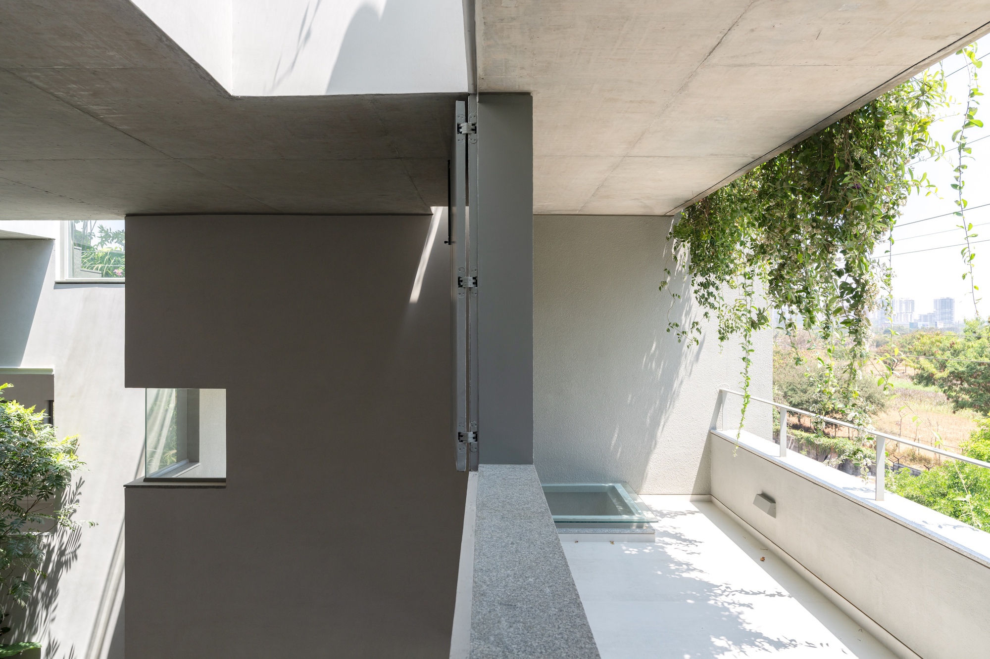 Covered terrace with exposed concrete ceiling, terrazzo flooring, and hanging vines filtering daylight