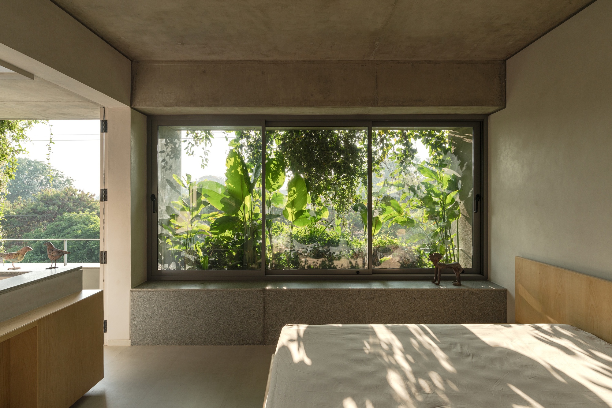 Bedroom window framing banana plants and tropical vegetation beyond a raised terrazzo planter bed