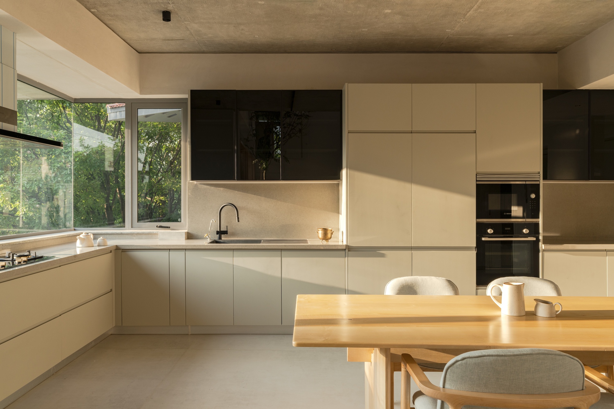 Kitchen with white cabinetry and timber dining table lit by afternoon sun through garden windows