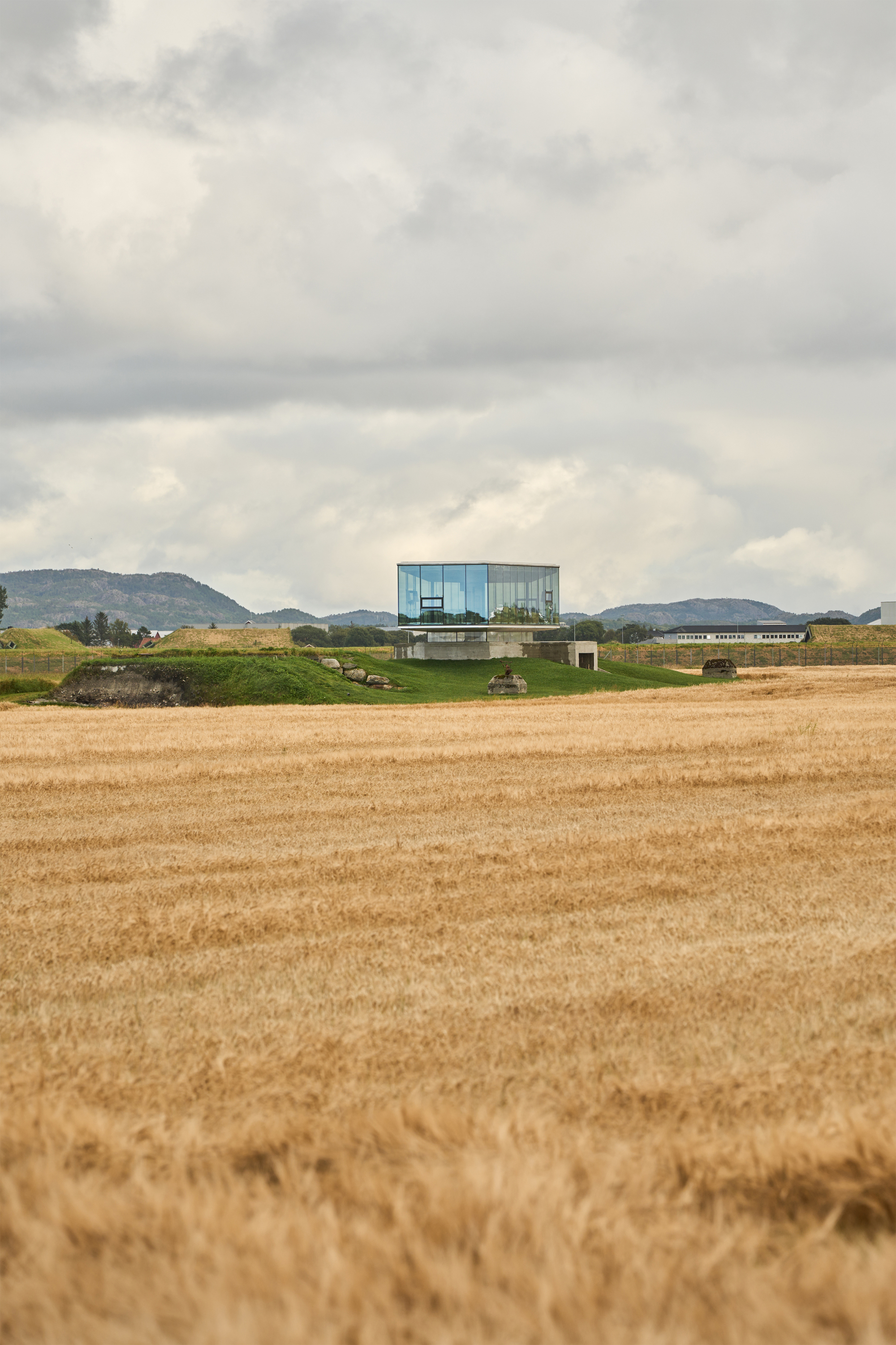 Distant view of the cantilevered structure in harvested fields beneath a heavy cloud cover and hills