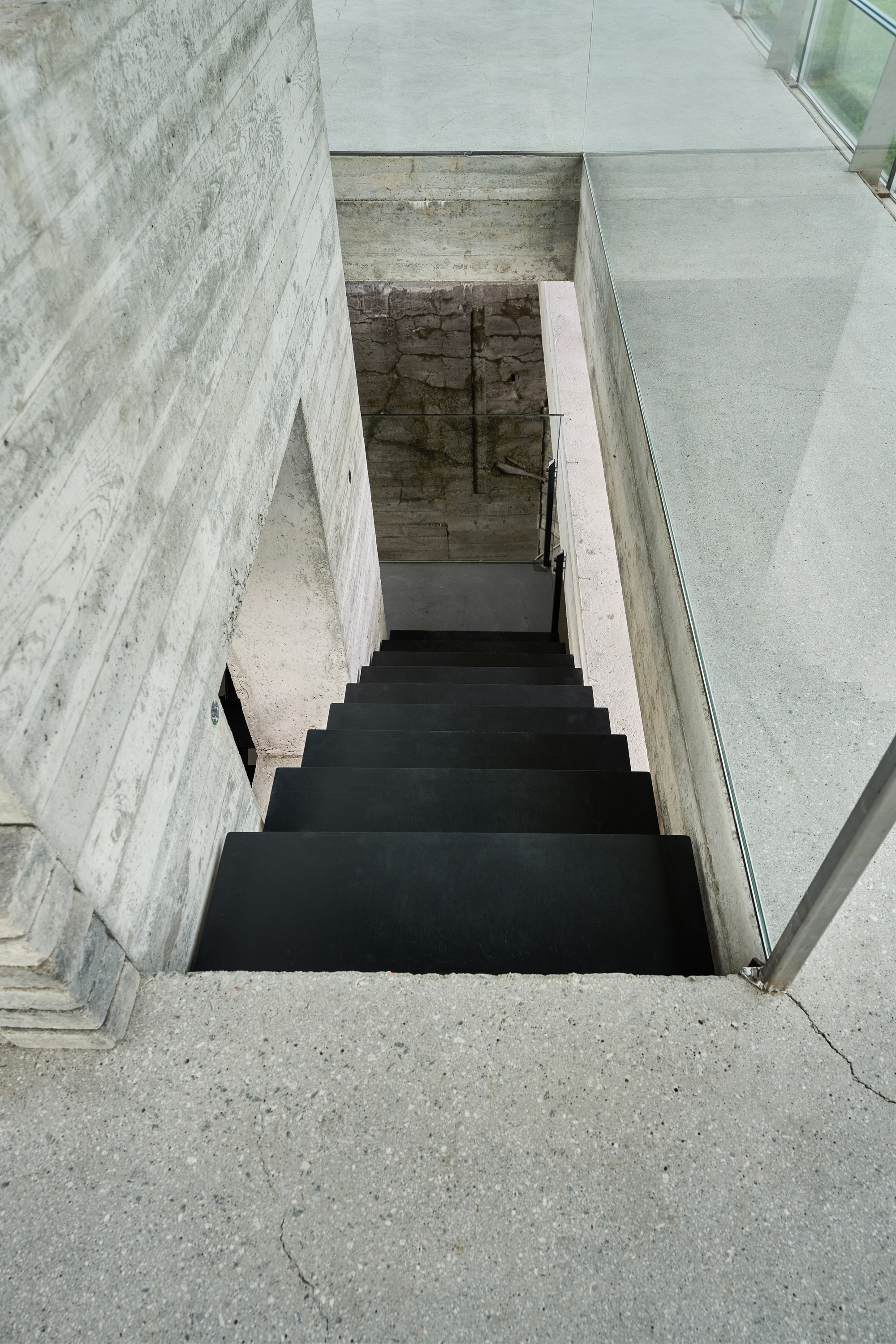 Top-down view of a steel staircase descending between board-formed concrete walls