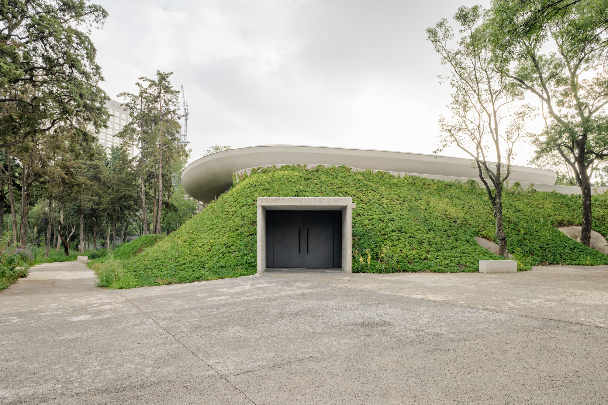 Entrance portal set into a planted earth berm beneath a curved cantilevered roof