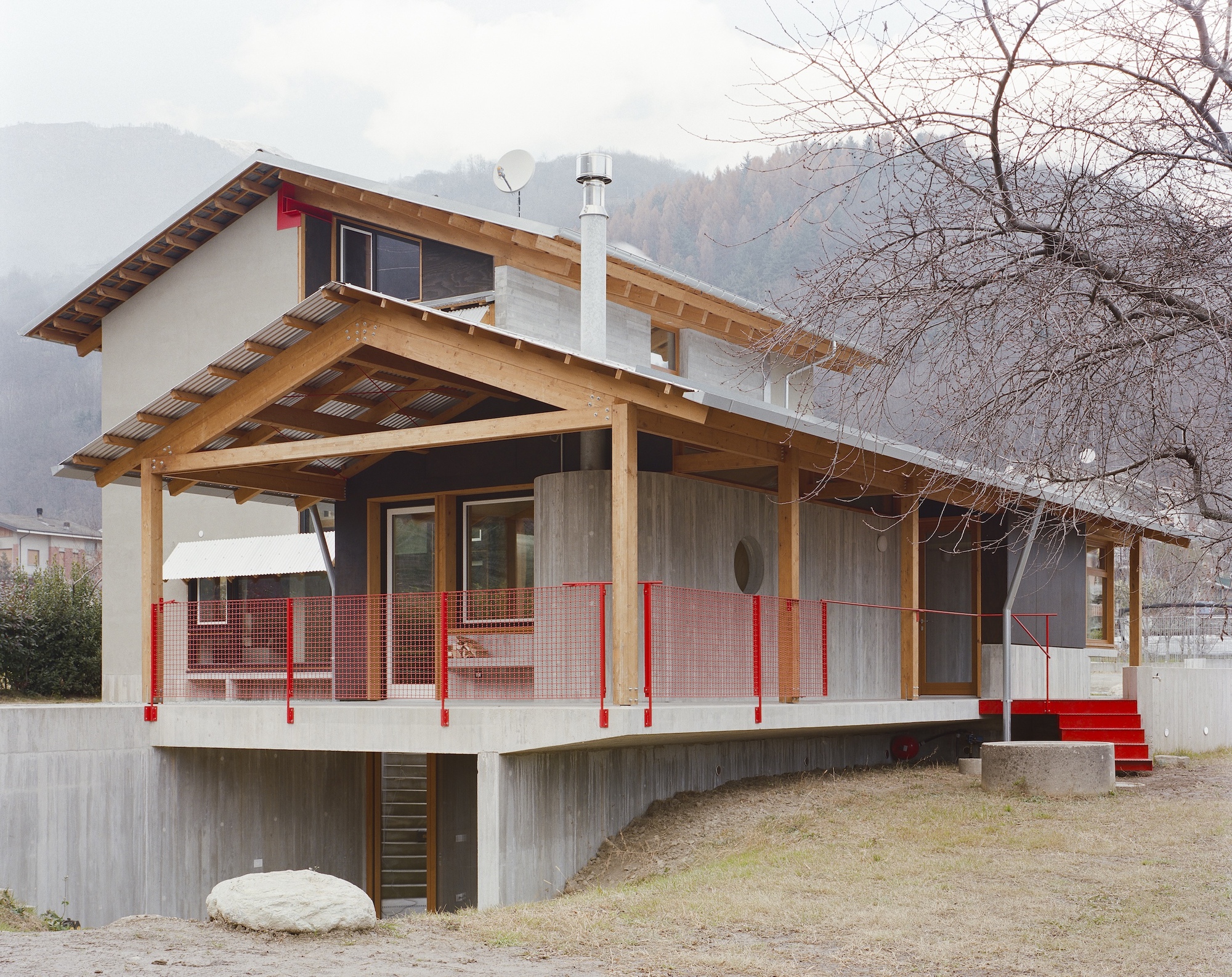 Elevated timber-framed porch with red mesh balustrade and corrugated metal skirting under bare tree branches