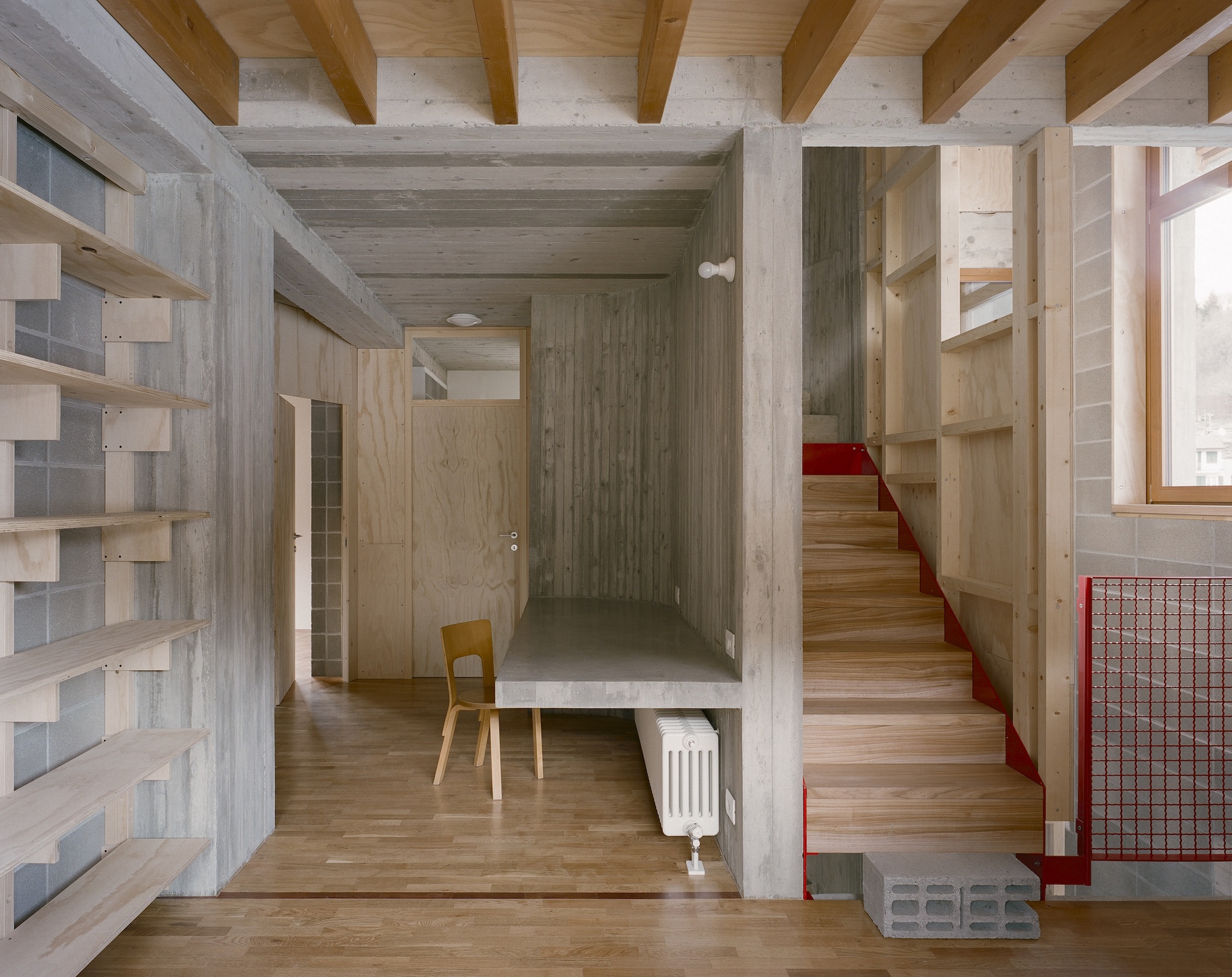 Entry hall with timber stair featuring red metal handrail and concrete structural frame