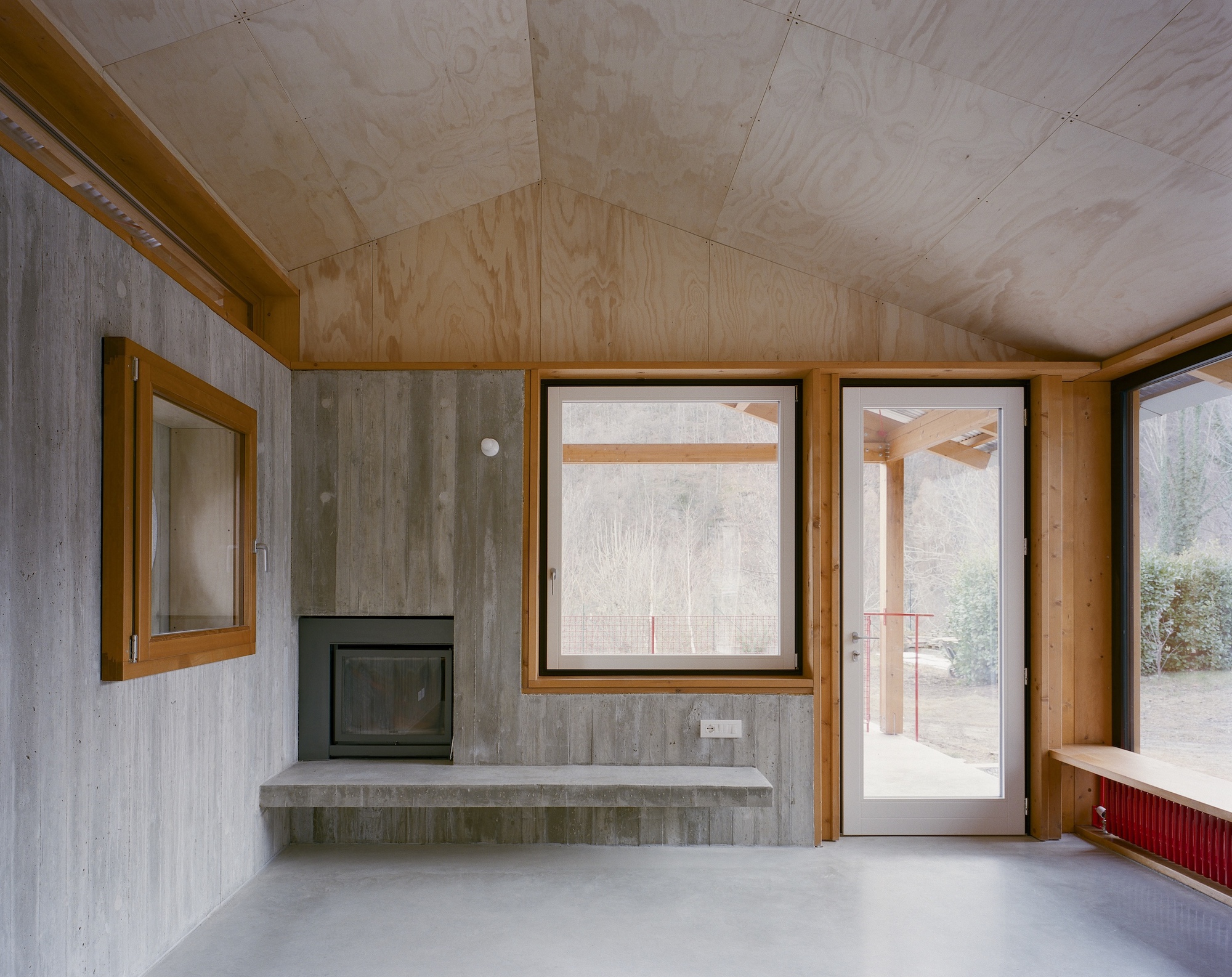 Interior room with plywood ceiling, board-formed concrete walls, and a corner fireplace