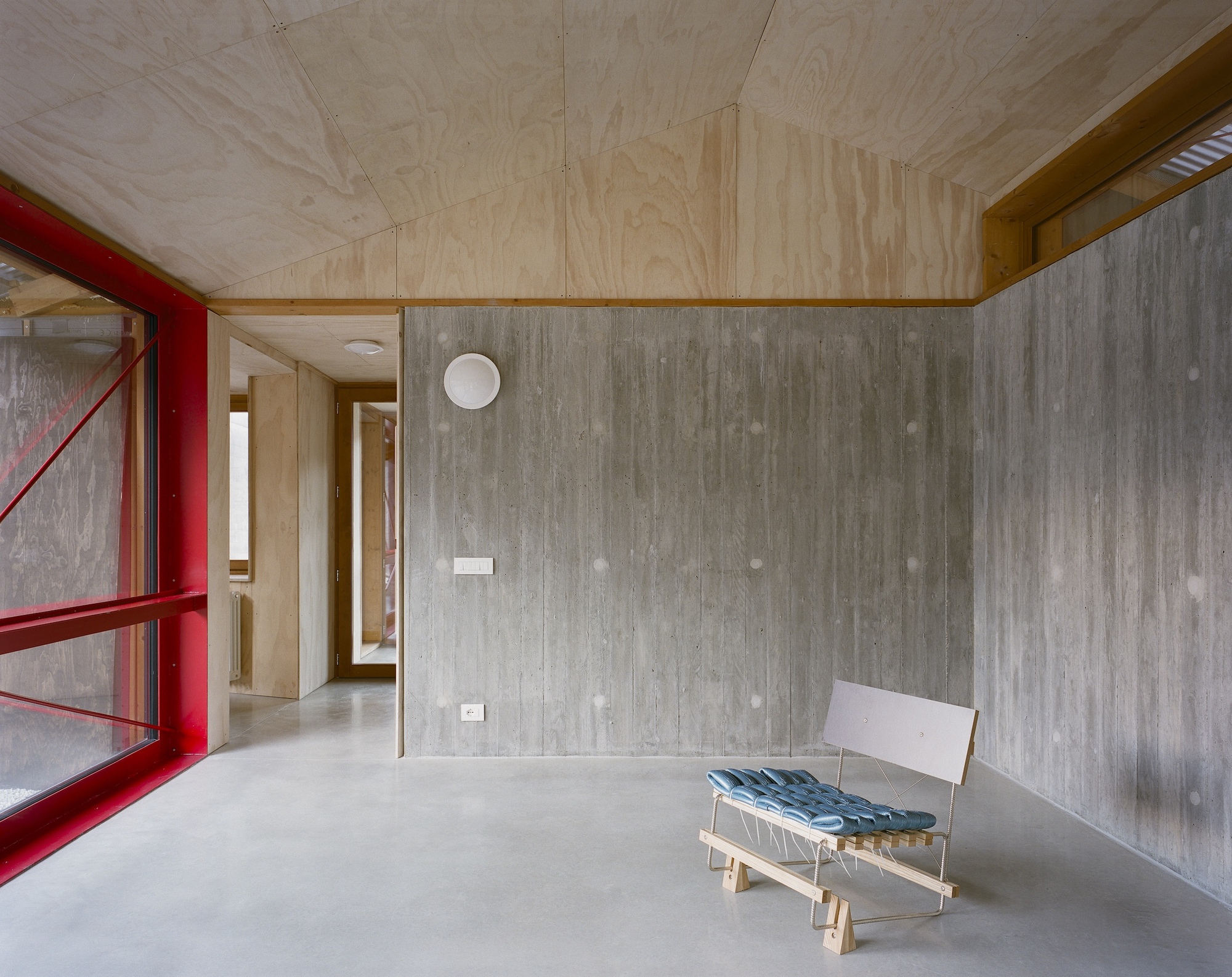 Living space with plywood ceiling and board-formed concrete walls featuring a lounge chair