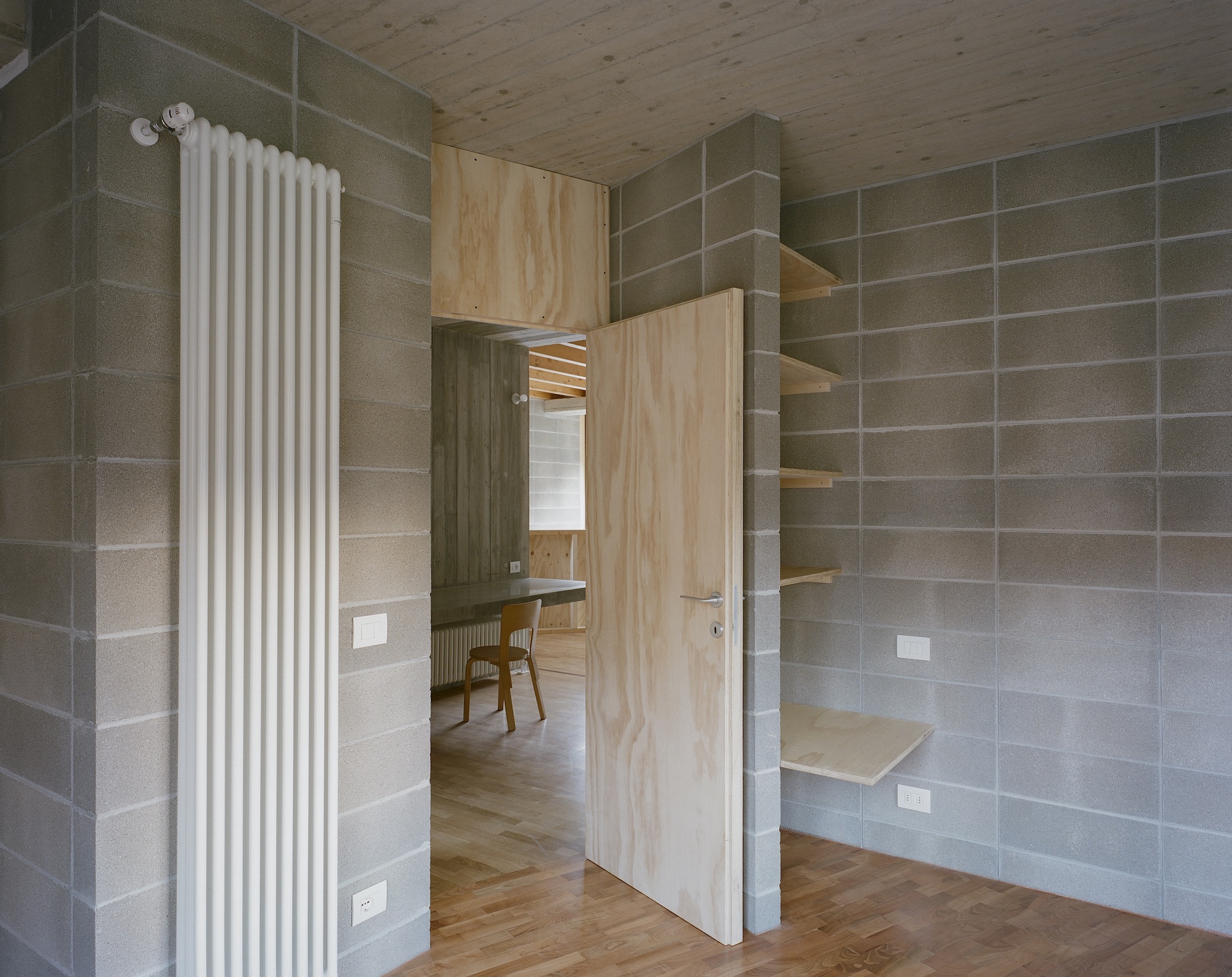 Interior room with concrete block walls, light plywood built-in shelving, and a white vertical radiator