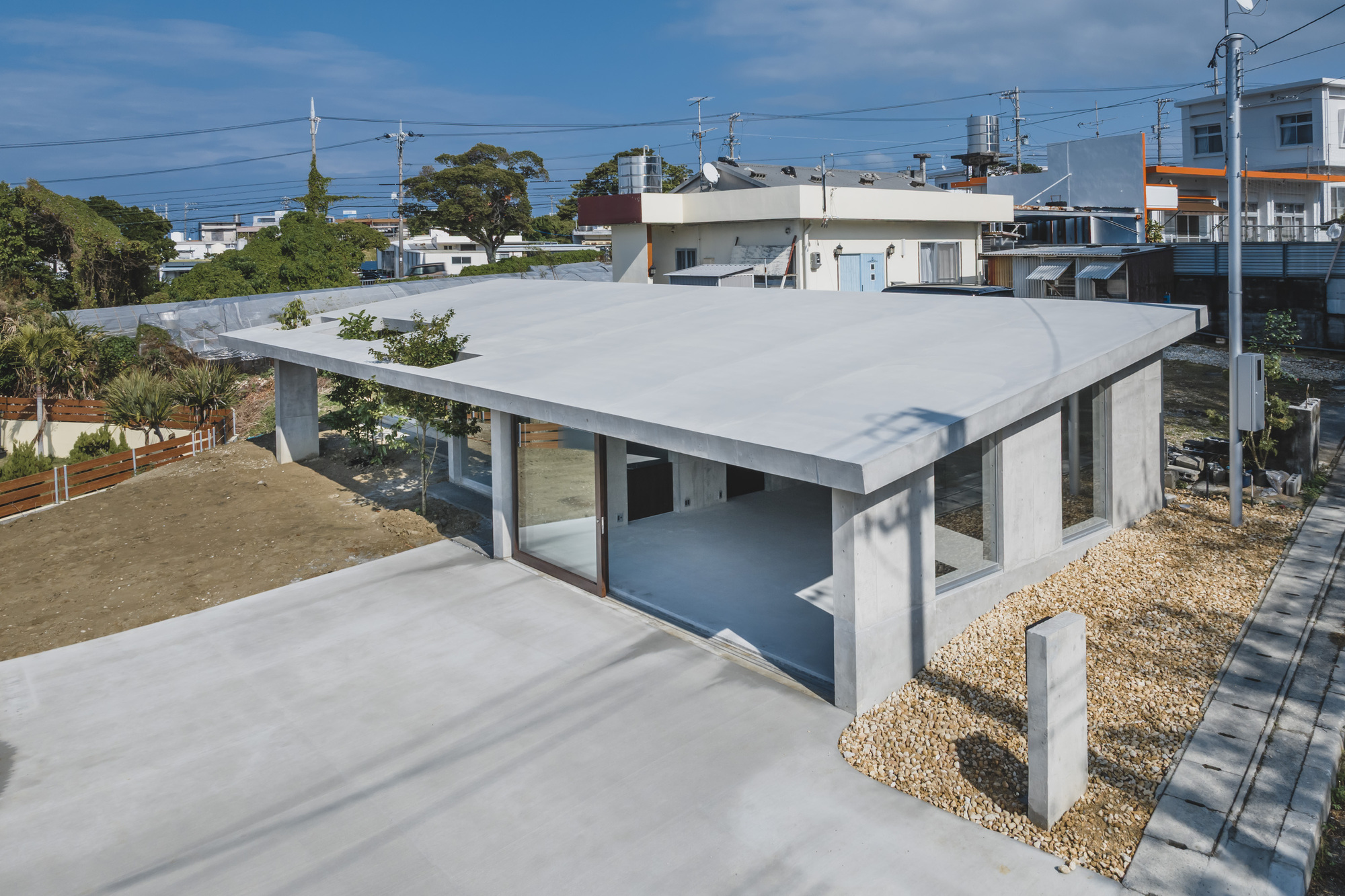Corner view showing the elevated concrete roof plane supported by cylindrical columns over gravel ground