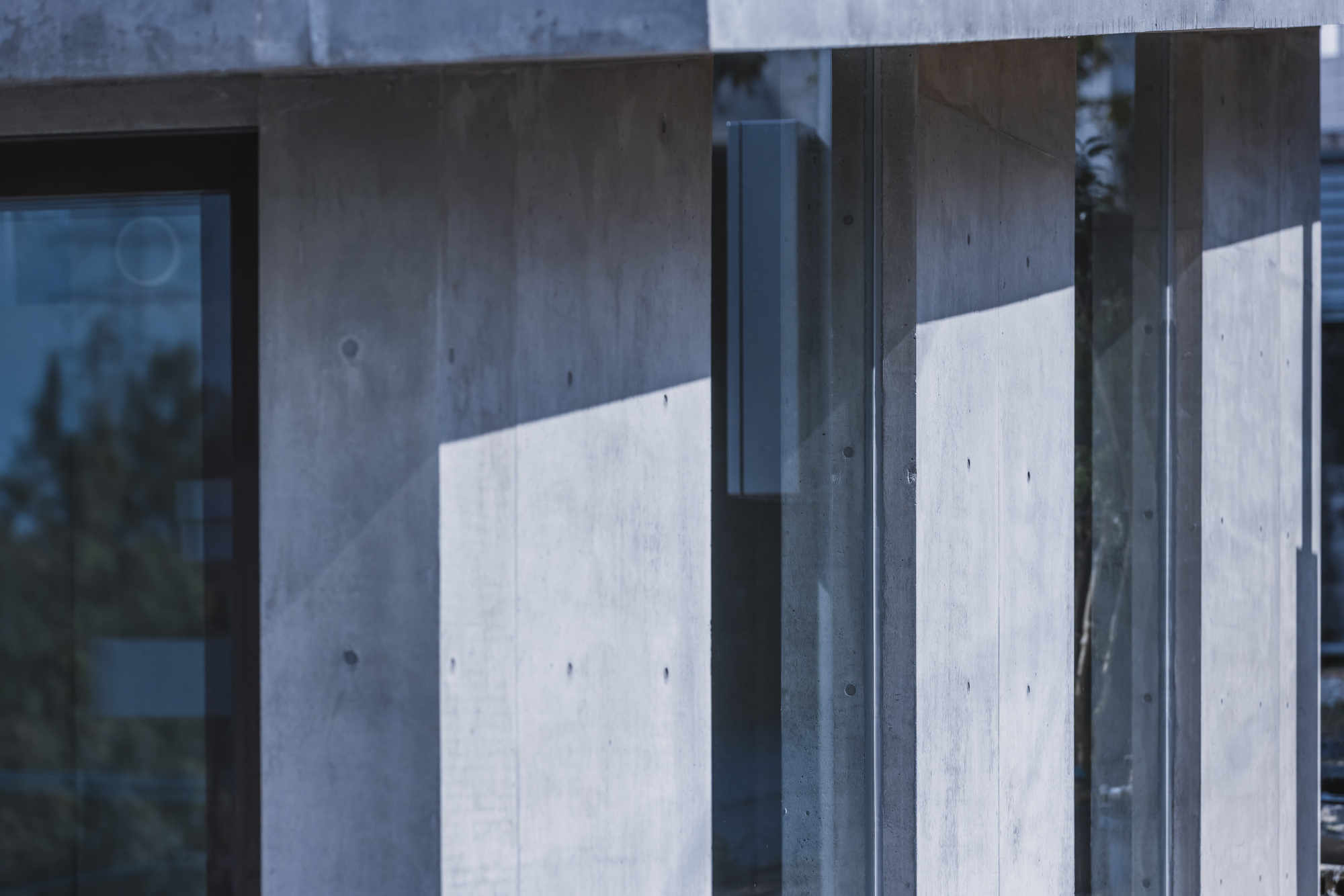 Close-up of concrete walls intersecting with steel-framed glass panels reflecting afternoon light