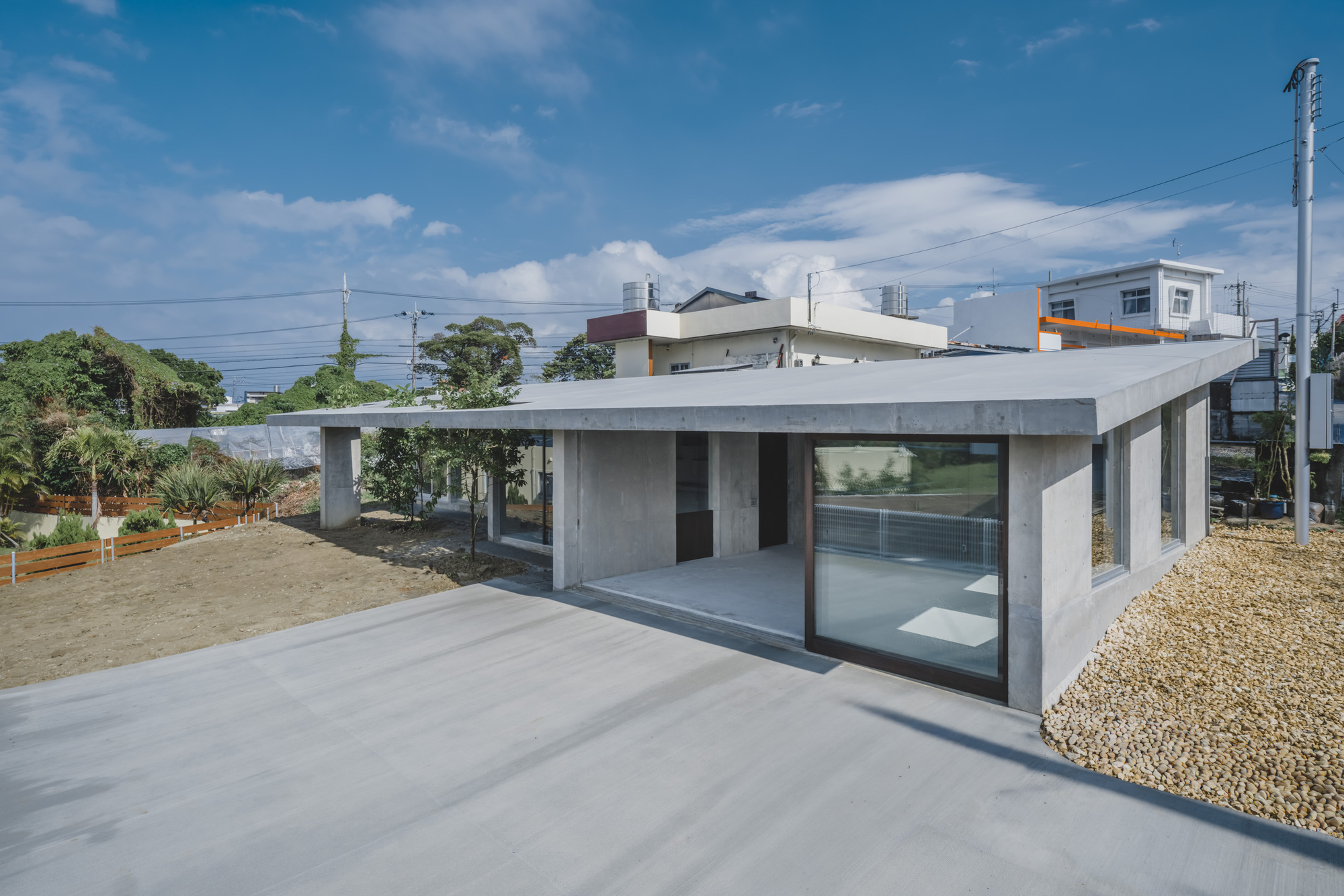 Single-story concrete pavilion with flat roof and glass walls overlooking a gravel courtyard
