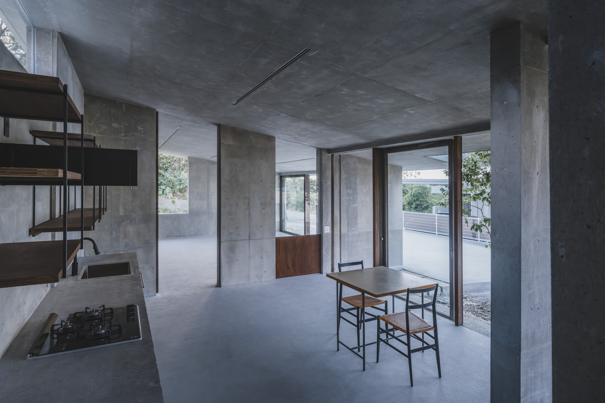Open plan interior with concrete columns and ceiling, dining table near glazed doors opening to courtyard
